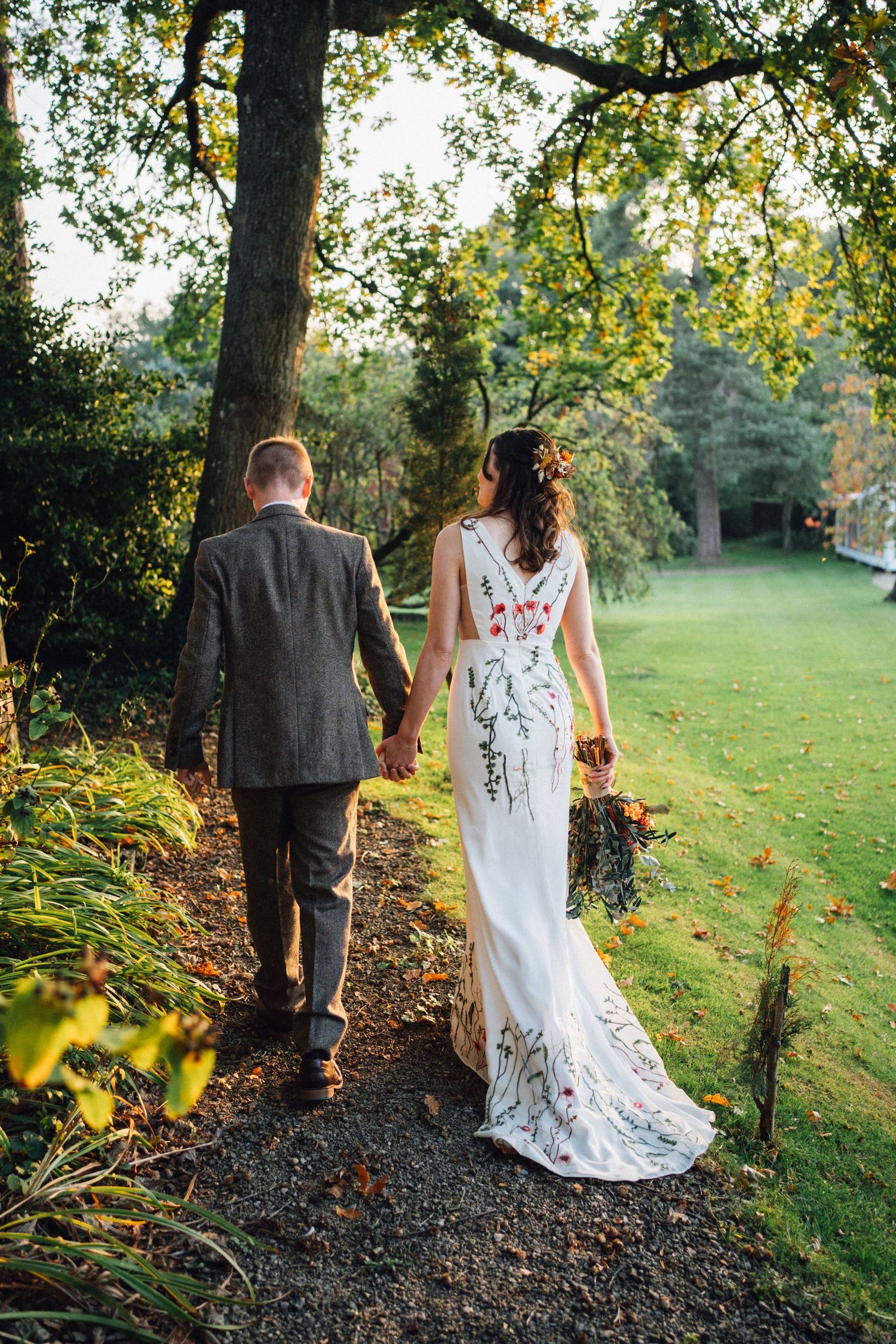 Romantic couple walking along a tree-lined path during golden hour at their outdoor wedding.