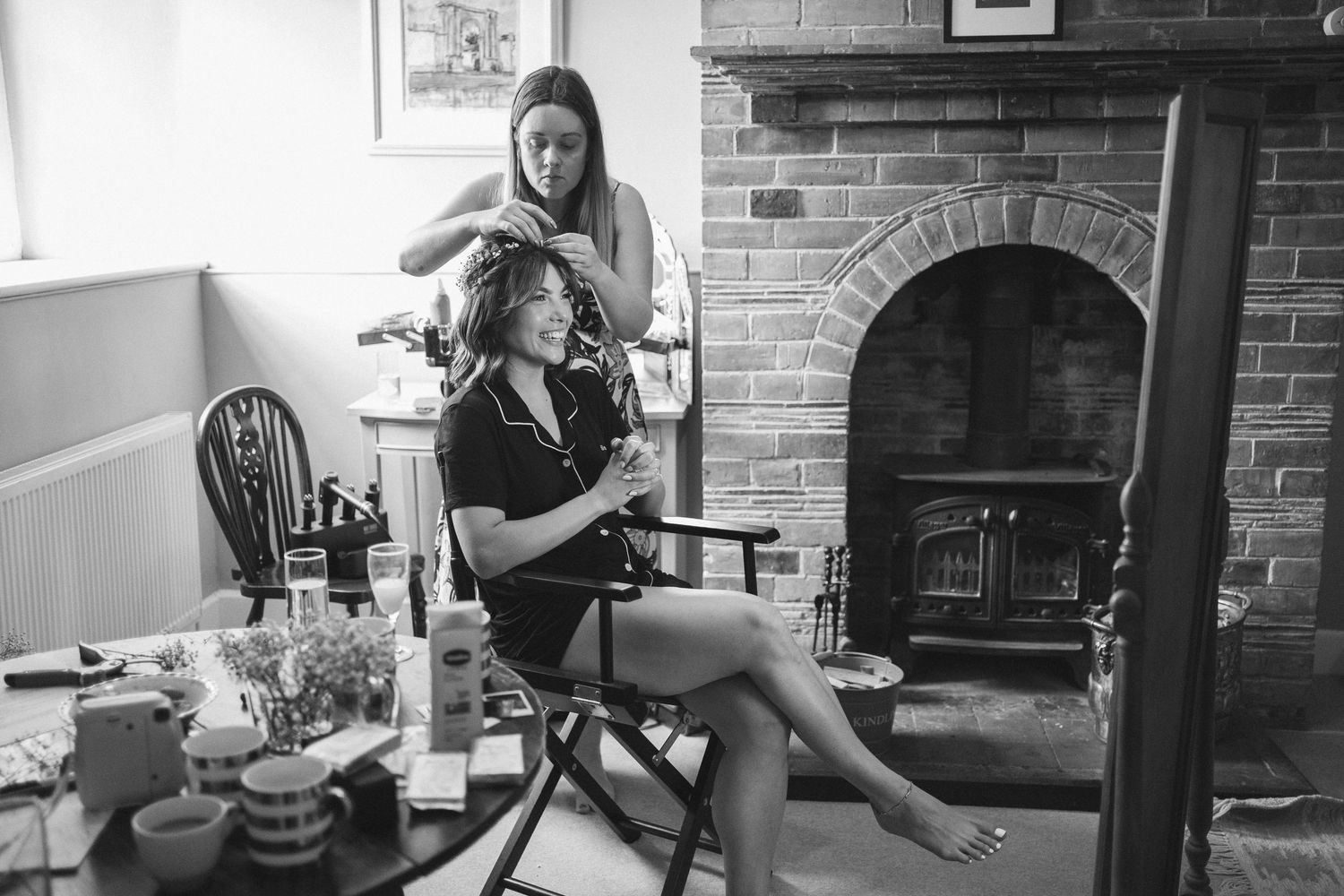 Black and white photo of wedding preparations in a rustic room with brick fireplace.
