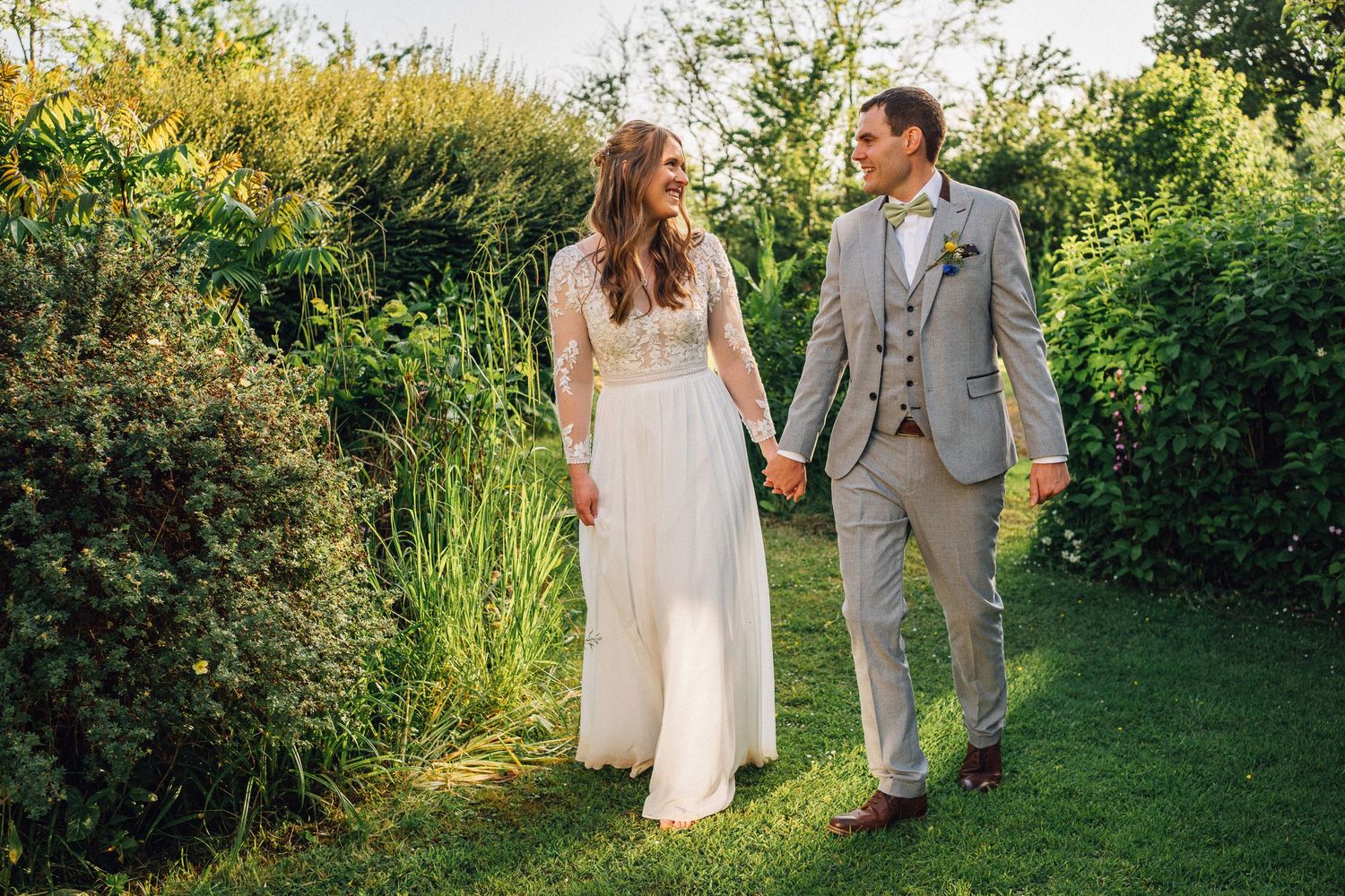 Couple strolls hand in hand through lush garden pathway during wedding photoshoot.