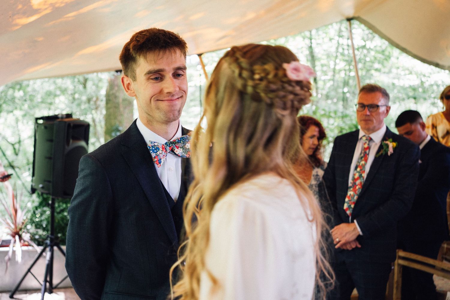 A wedding ceremony moment under a white tent with guests gathered around.