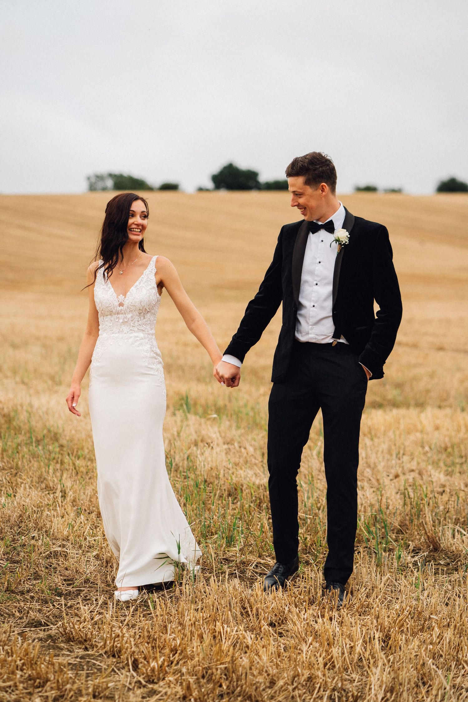 Newlyweds playfully walking through a golden wheat field during sunset photo session.