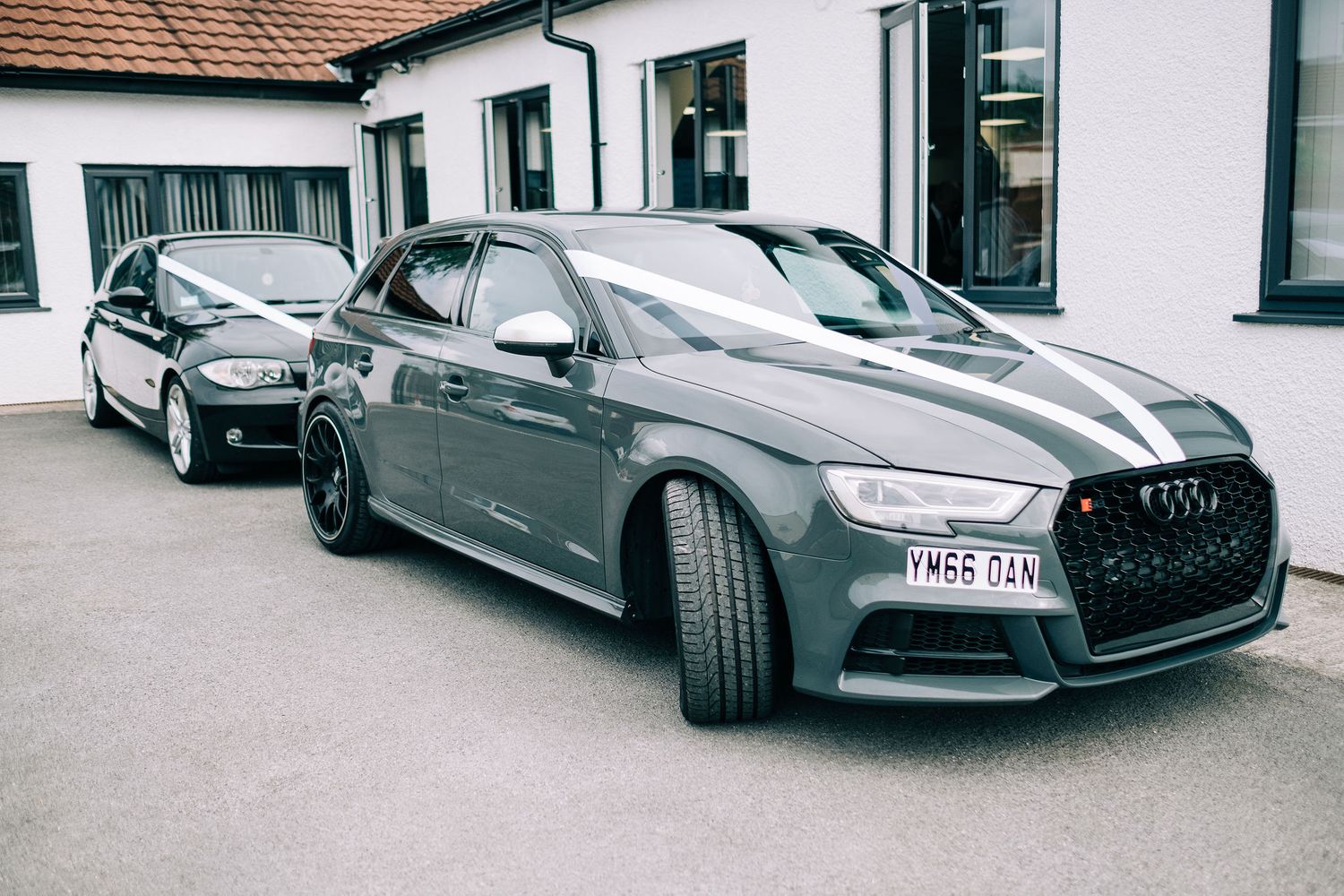 Luxury cars parked outside a white building with traditional tile roofing.