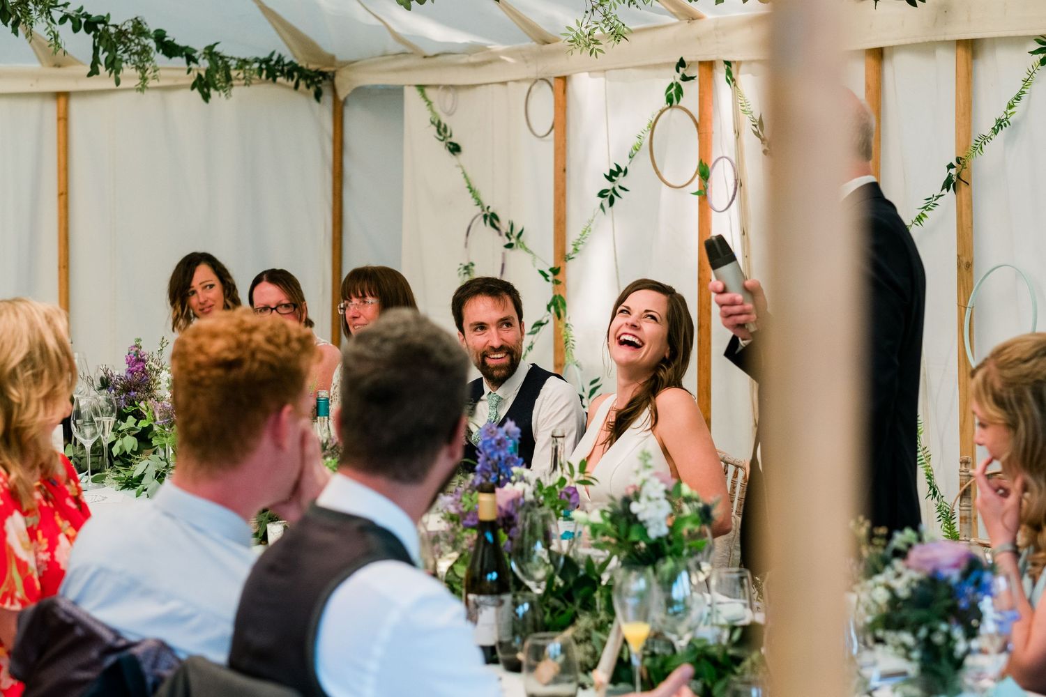 Wedding guests mingling and socializing at decorated reception tables under a white tent canopy.