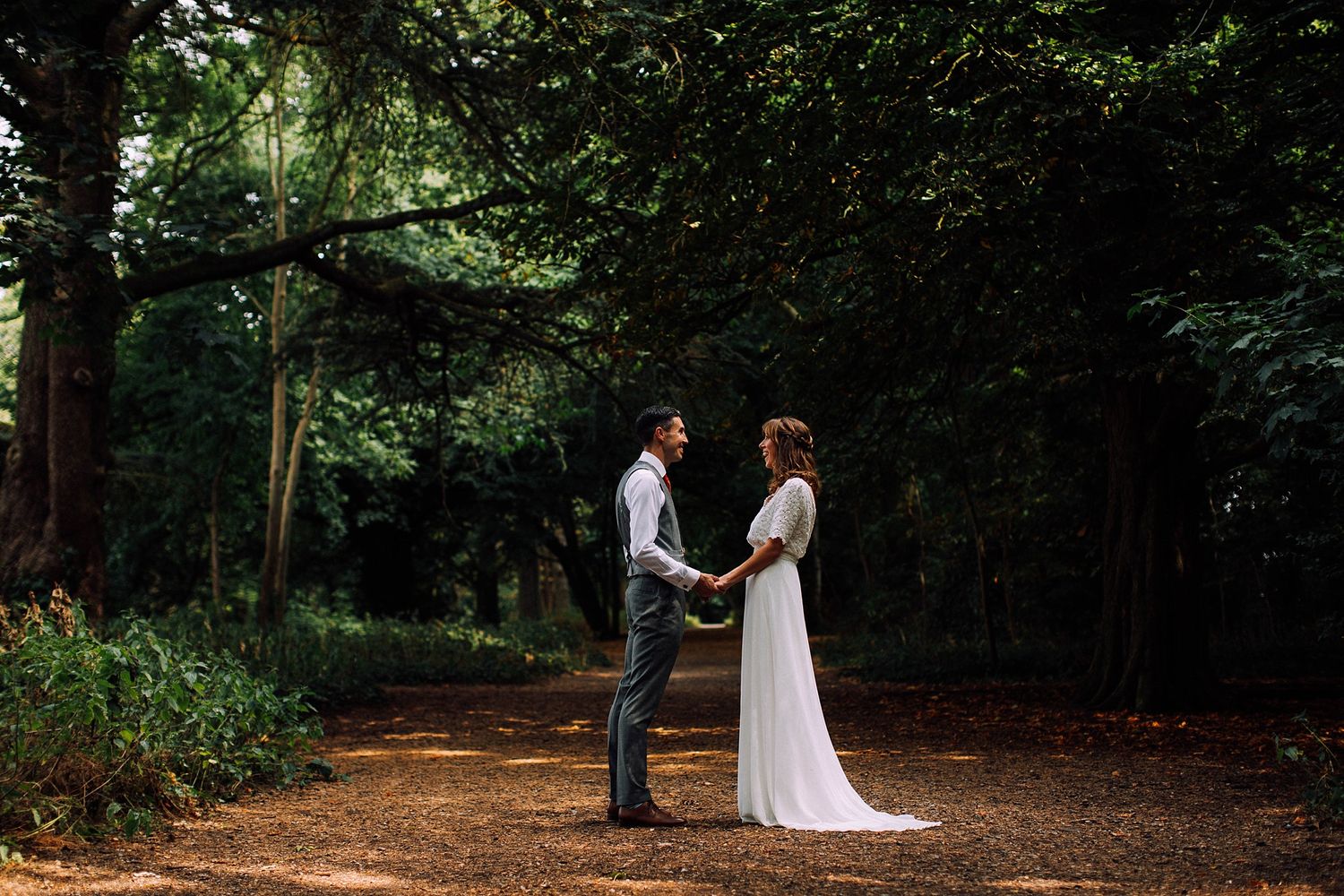 A wedding couple stands together on a forest path surrounded by lush greenery.