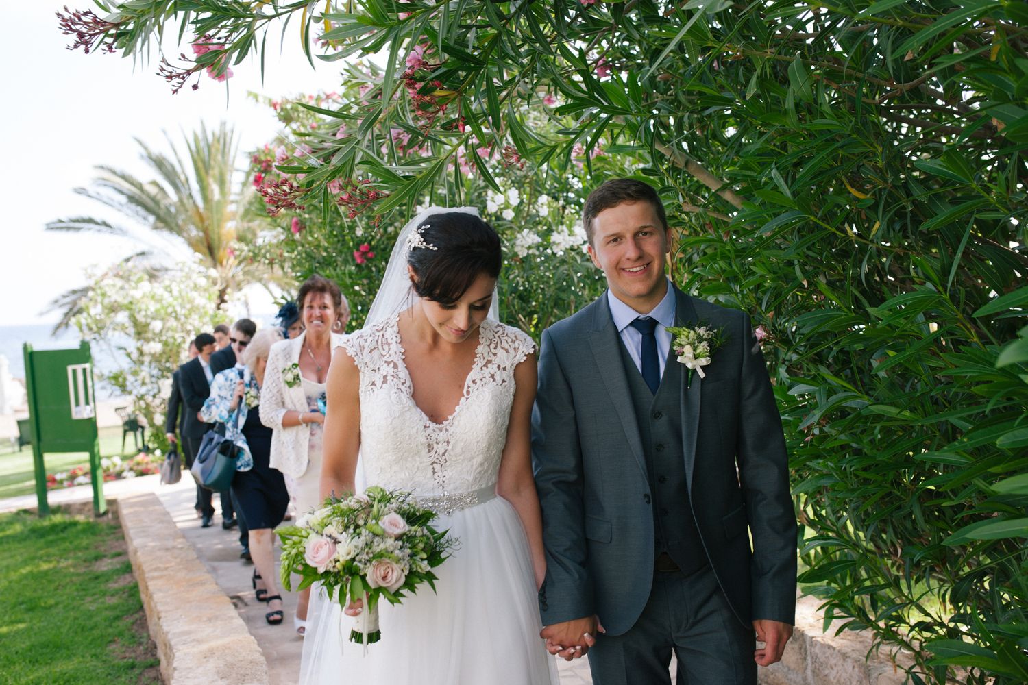 A wedding procession along a palm-lined pathway with guests following the newlyweds.