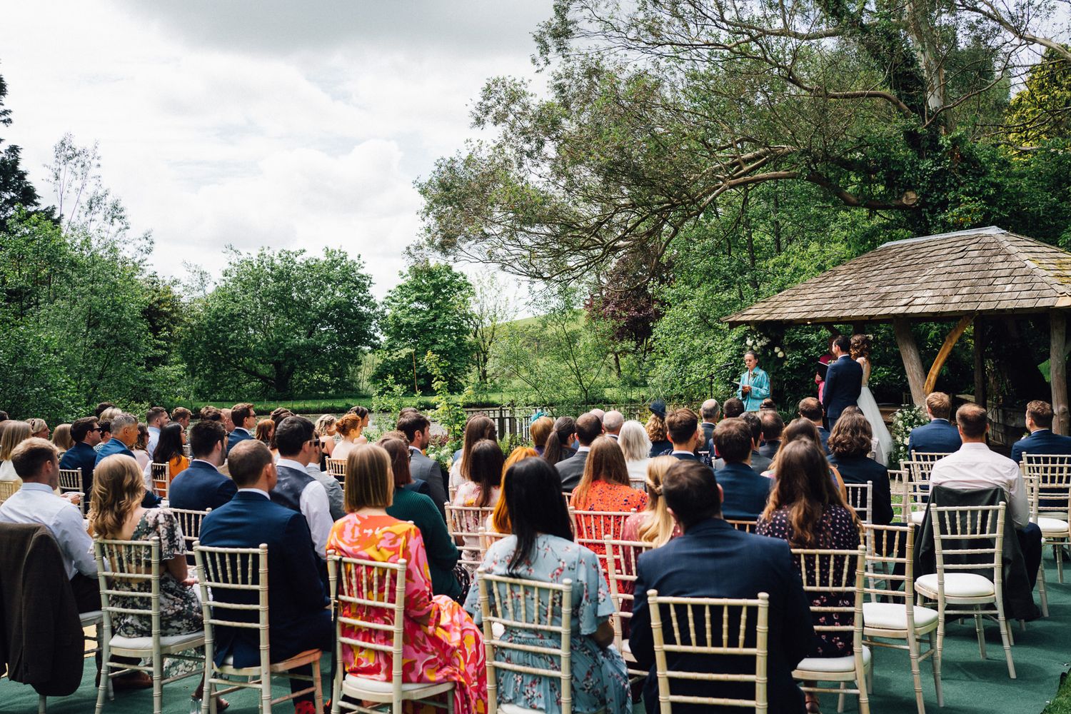 Guests seated in white chairs for an outdoor wedding ceremony under cloudy skies.