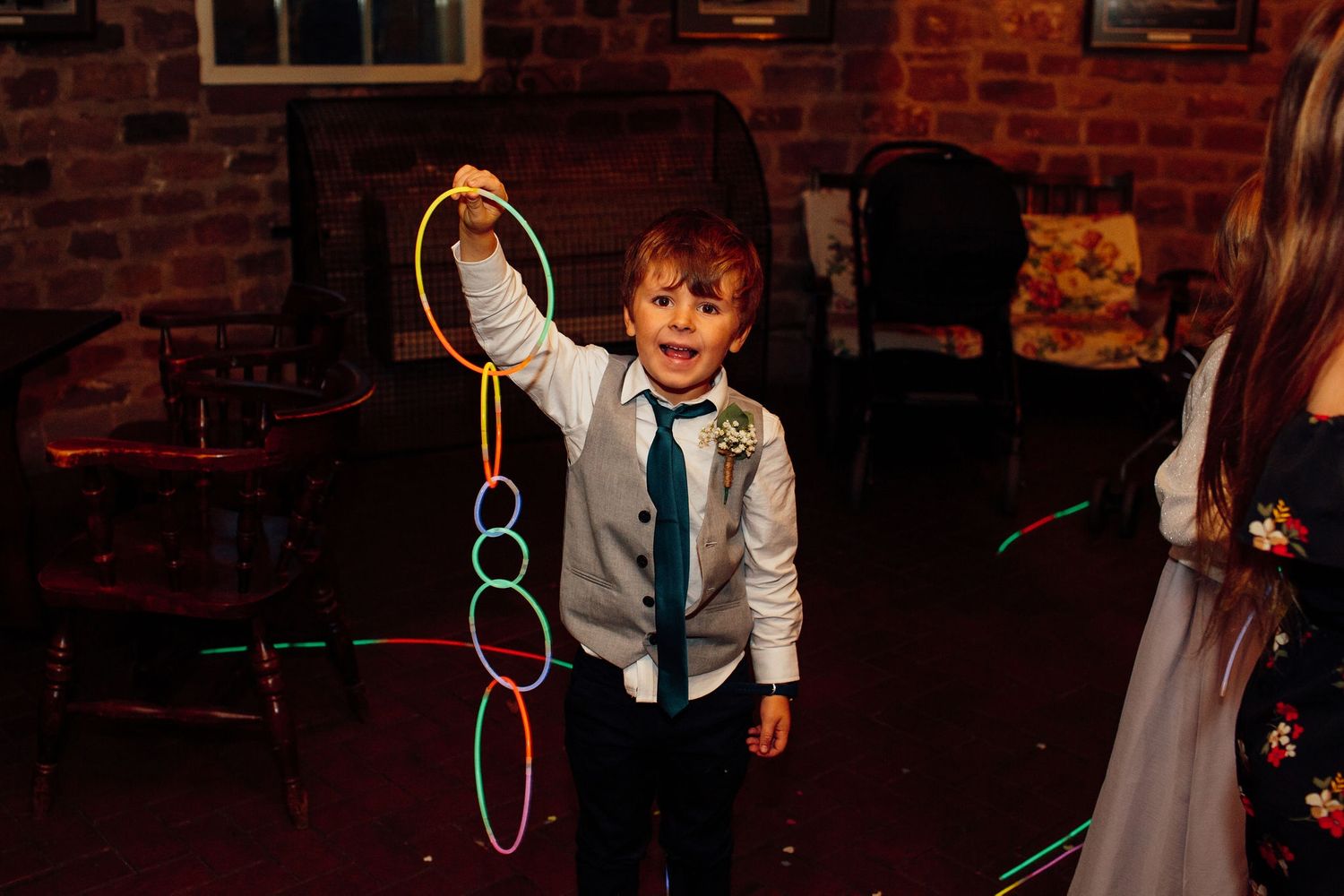 Children playing with colorful bubble wands at a wedding reception against brick wall backdrop.