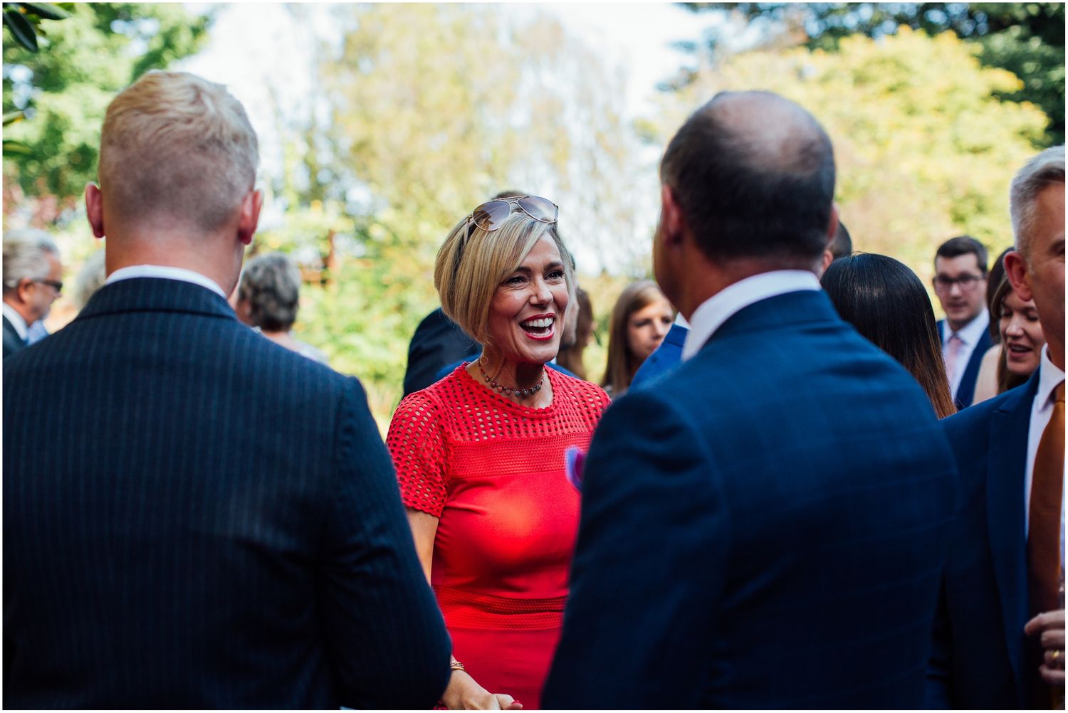 Wedding guests in formal attire sharing laughs during outdoor reception.