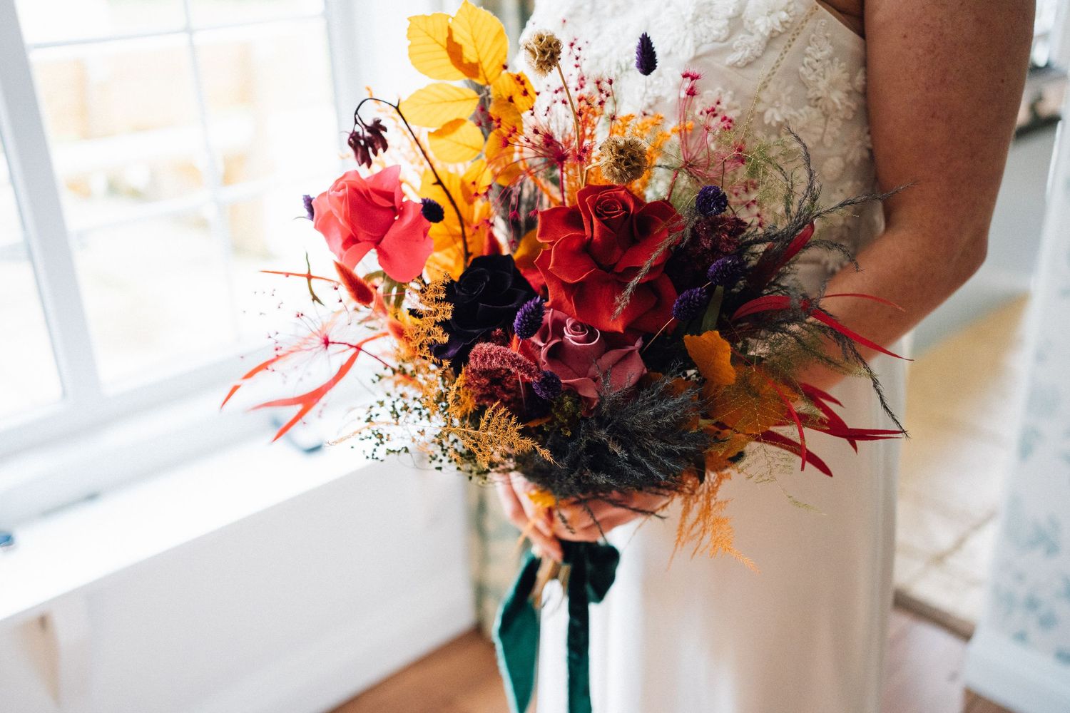 Autumn-themed wedding bouquets featuring orange, red and burgundy flowers with dark accents and dried elements.