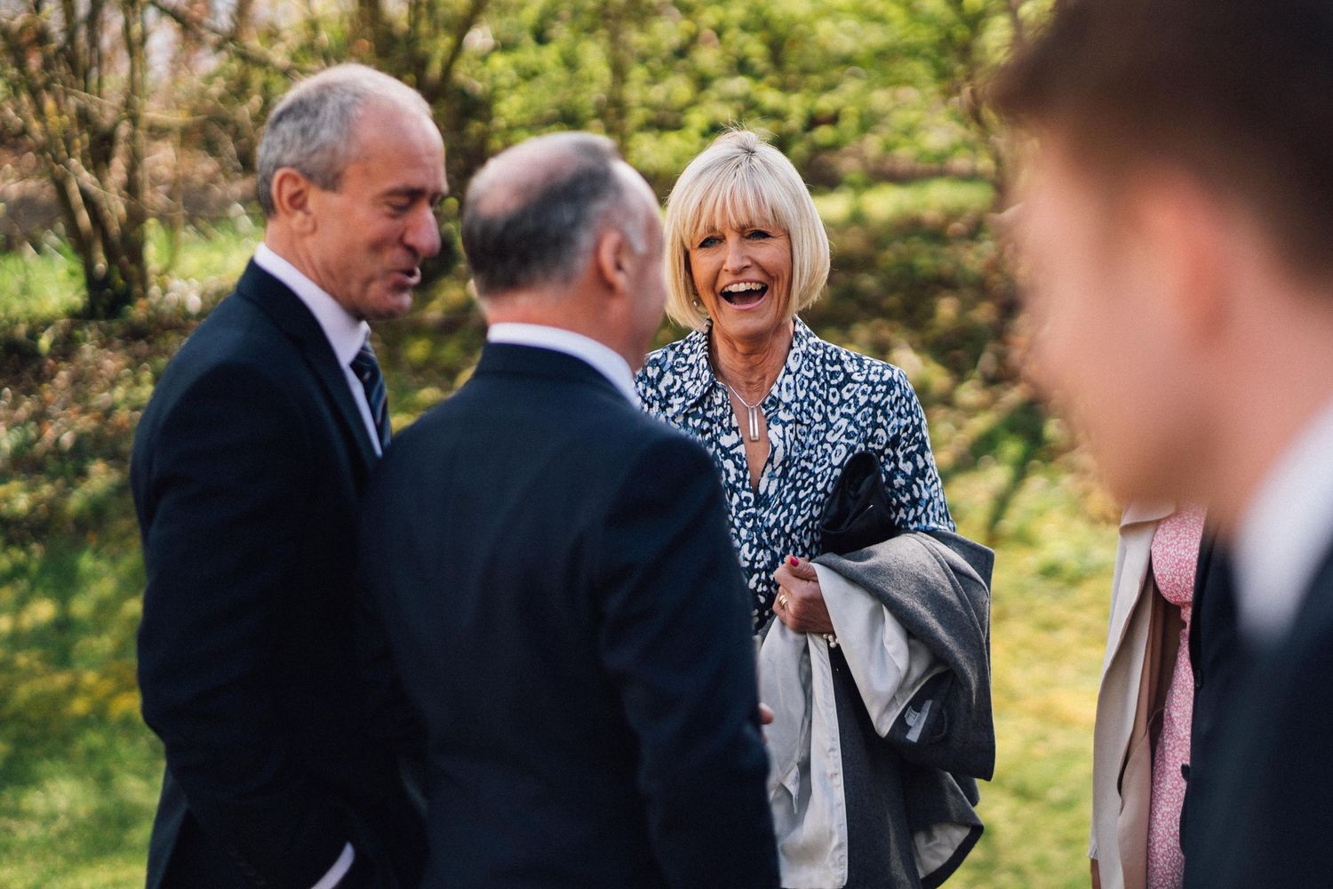 A group of people share a joyful moment together outdoors on a sunny day, with natural greenery in the background.