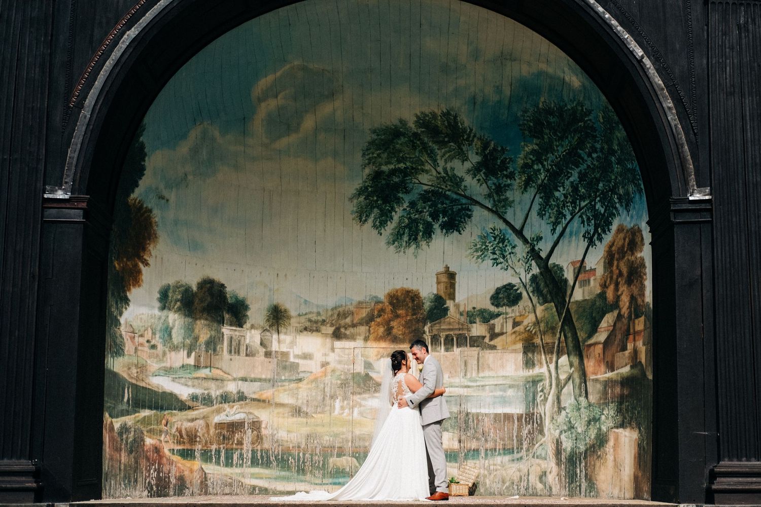 Romantic wedding portrait under an ornate archway with vintage mural backdrop.