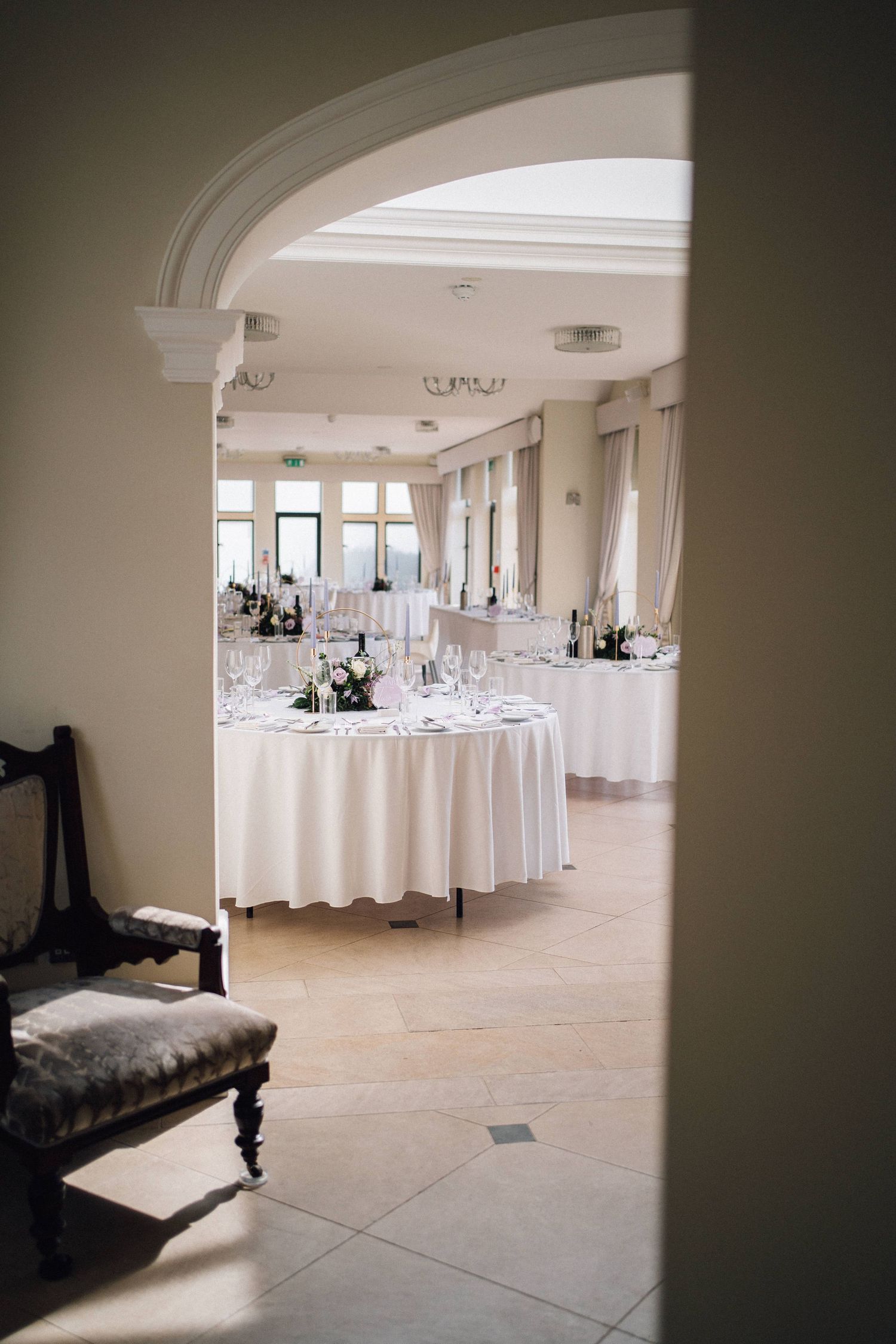 White banquet hall setup with round tables and elegant decor viewed through an arched doorway in a modern venue.