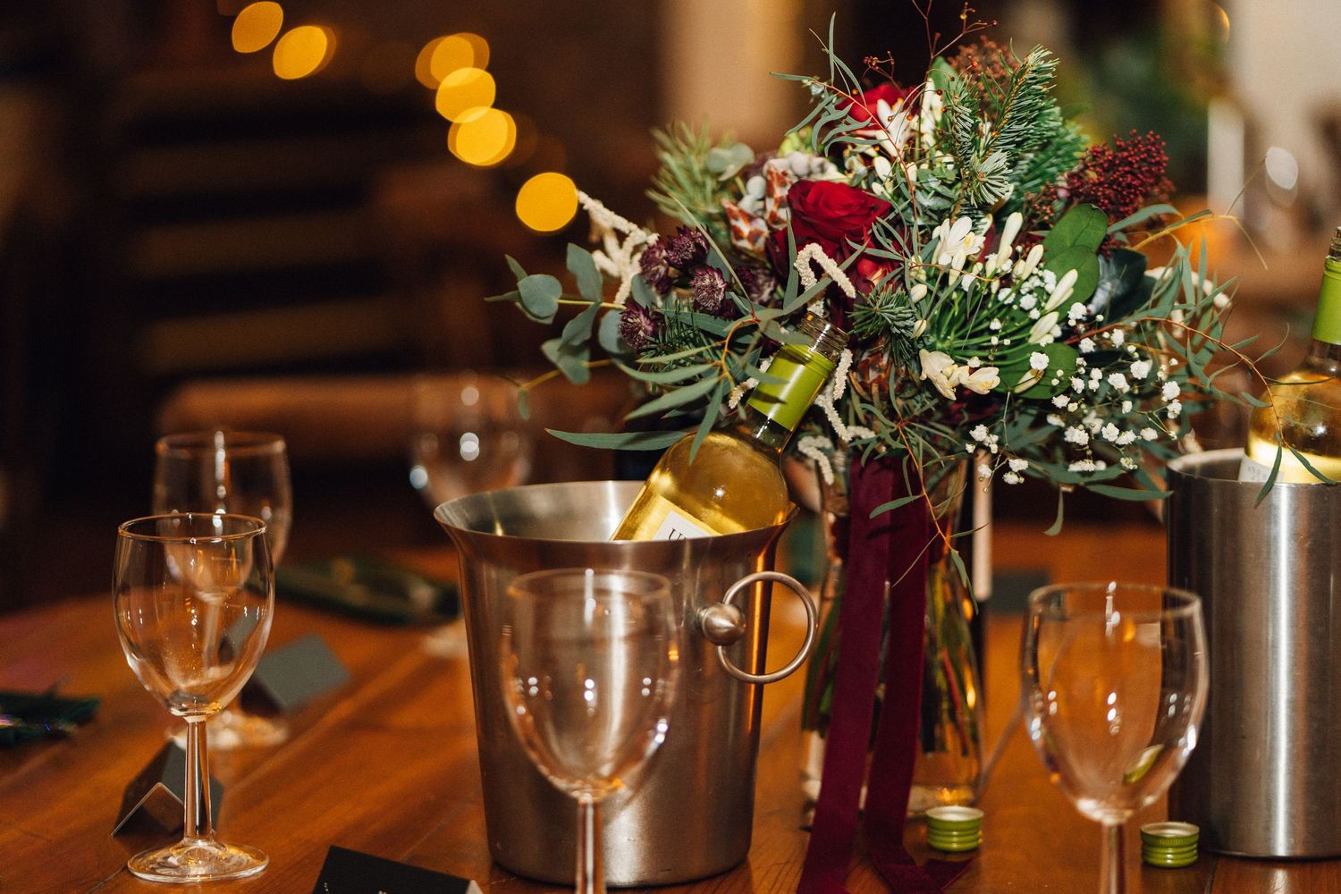 Elegant table setting with wine glasses and floral centerpieces illuminated by warm bokeh lights in a restaurant.