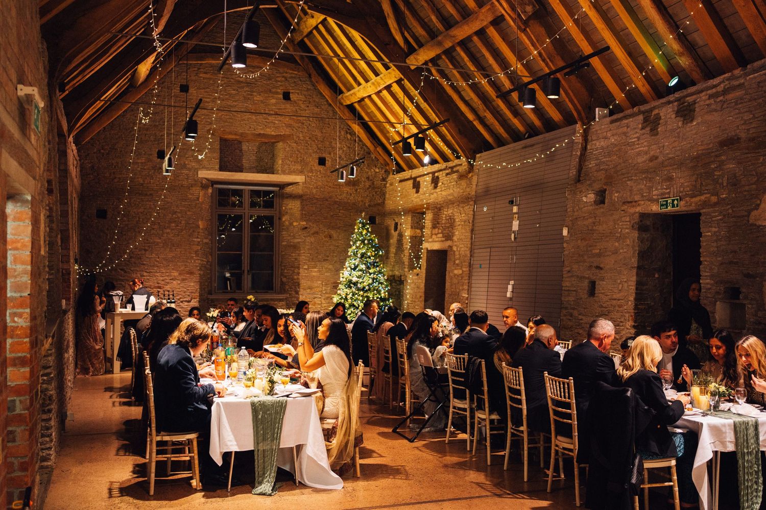 A rustic barn wedding reception venue with exposed wooden beams and soft lighting creates a warm, romantic atmosphere.
