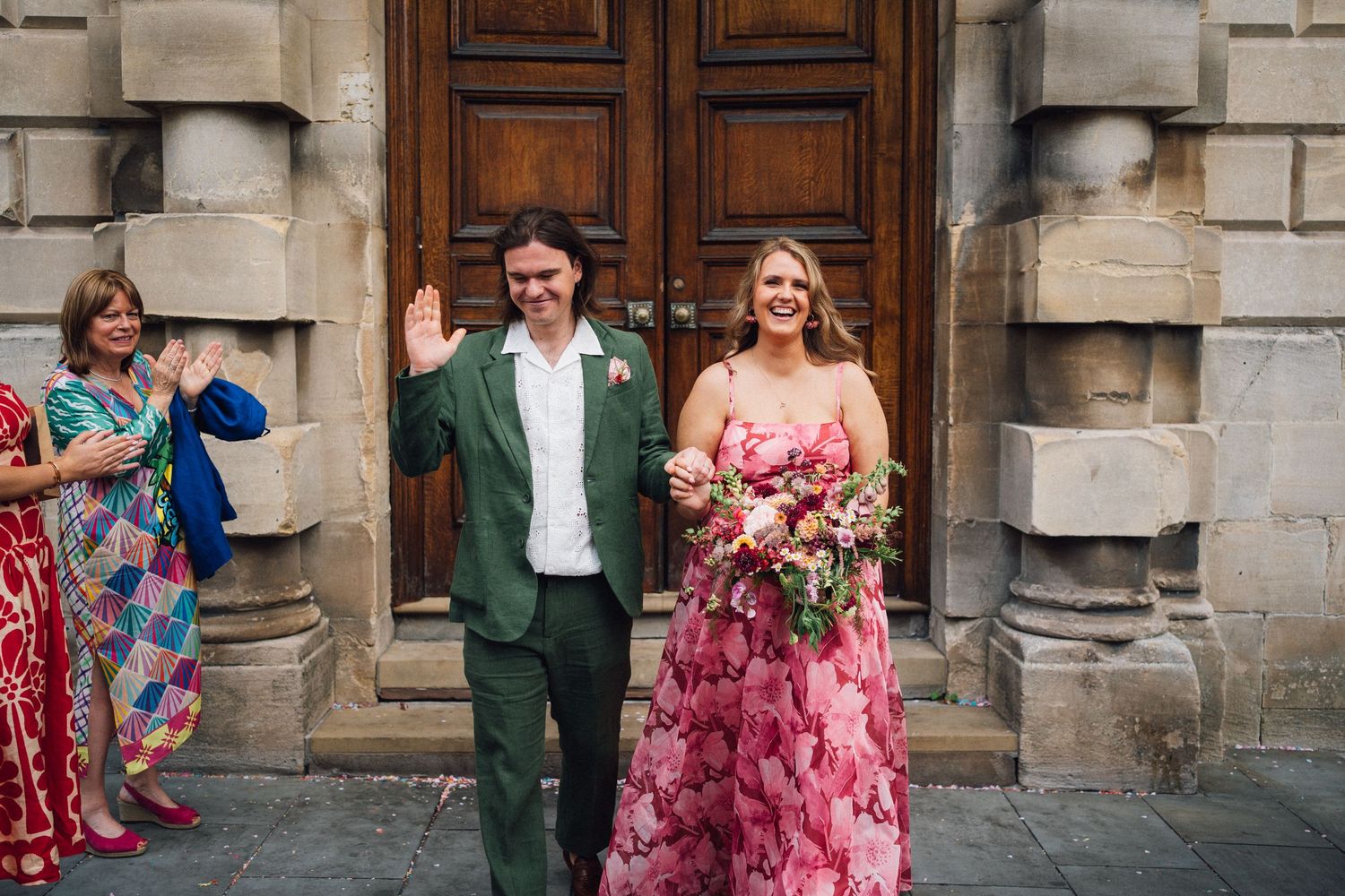 Wedding party guests gather on stone steps outside a historic building during a celebration.