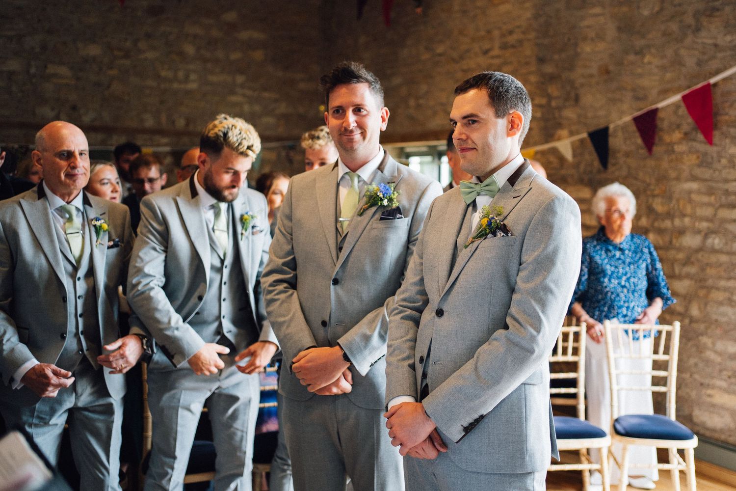 Groomsmen in matching gray suits share laughs and smiles during a candid wedding party moment.