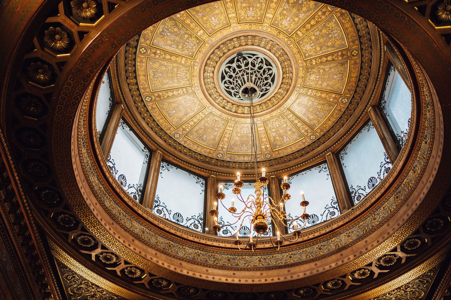 Ornate golden domed ceiling with intricate architectural details and a central skylight in a historic building interior.