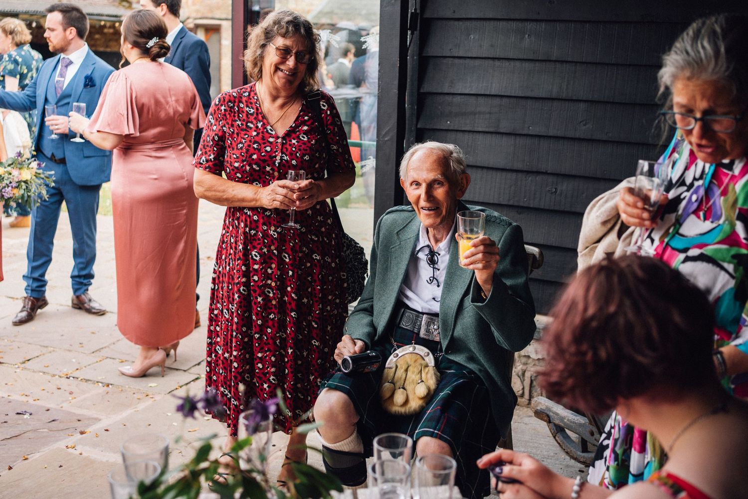 Wedding guests gather outdoors for a casual reception with drinks and conversation.