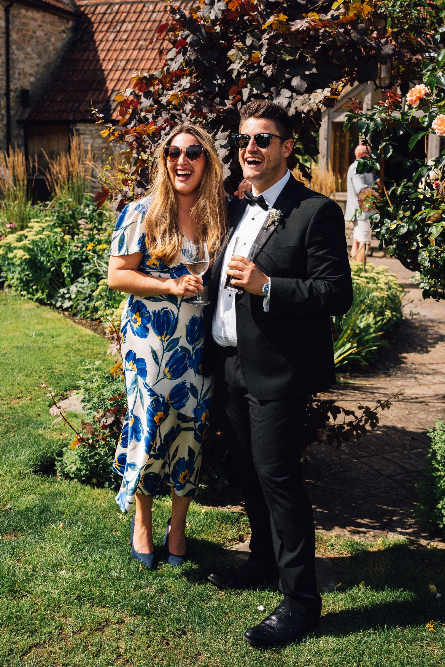 Couple enjoying drinks and laughter in a sunny garden setting.