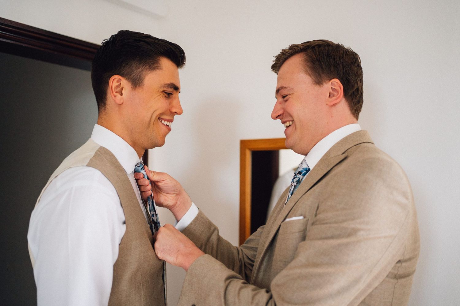 Men in formal attire help each other prepare and adjust their ties before the ceremony.