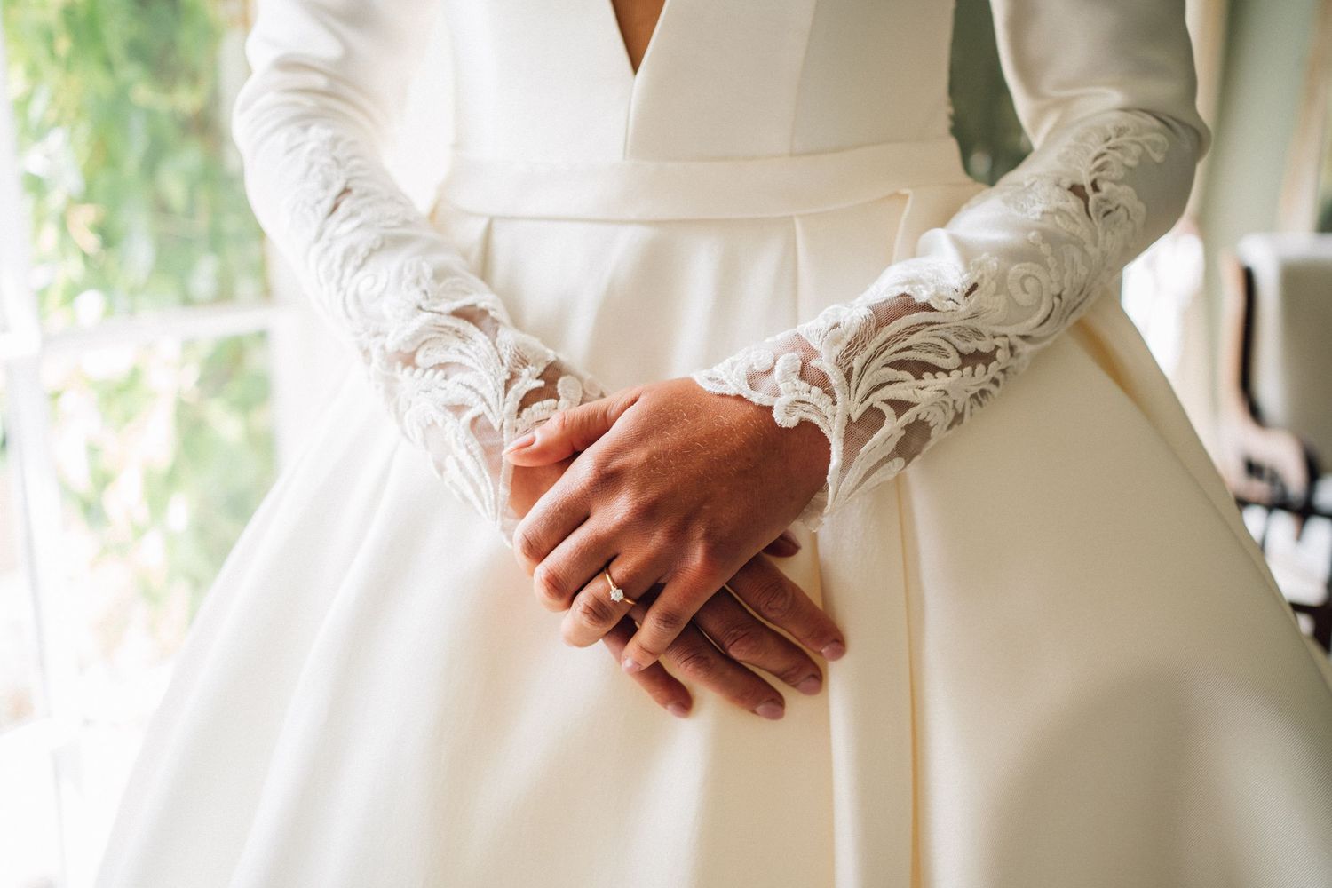 Close-up detail of lace sleeves and clasped hands on an elegant white wedding dress.