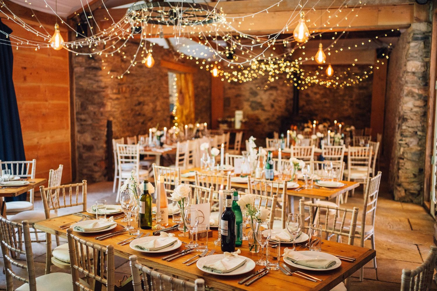 Wedding reception hall decorated with twinkling lights and white chairs in a stone-walled venue.