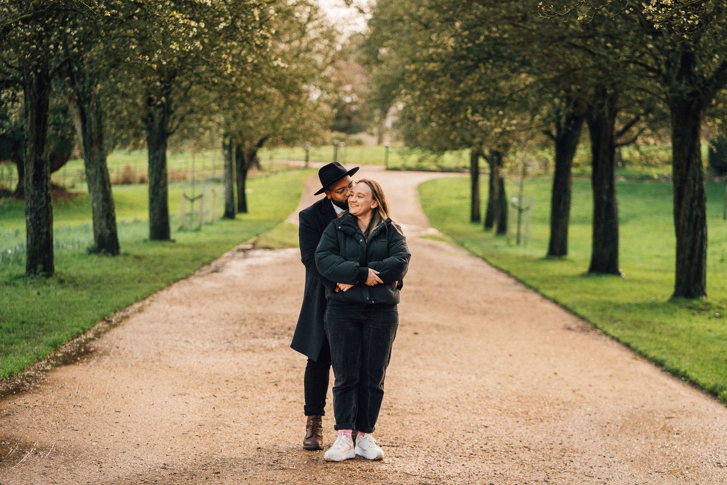 Two people walking together on a tree-lined path in a scenic park.