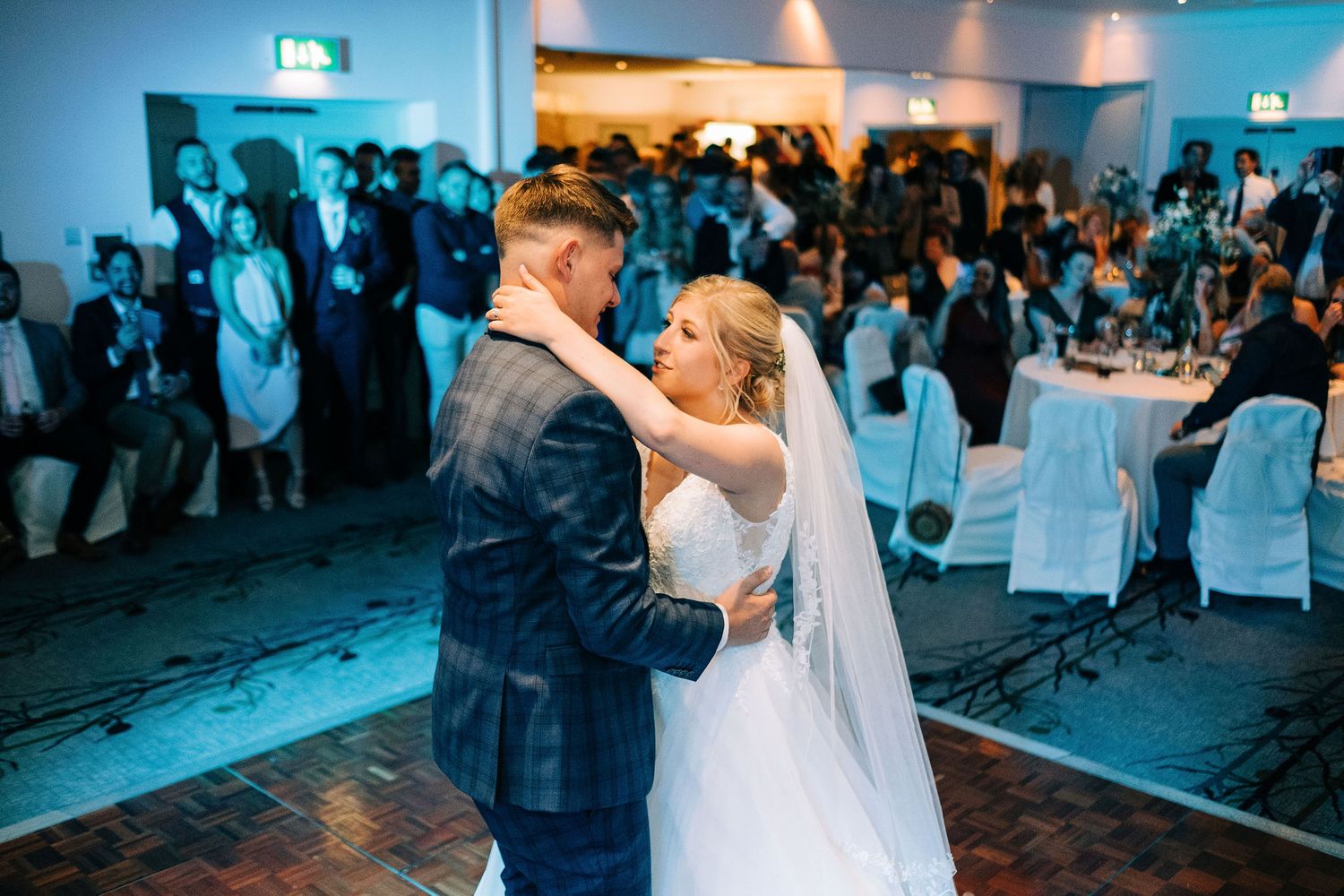 Wedding reception dance floor filled with guests under atmospheric blue lighting.