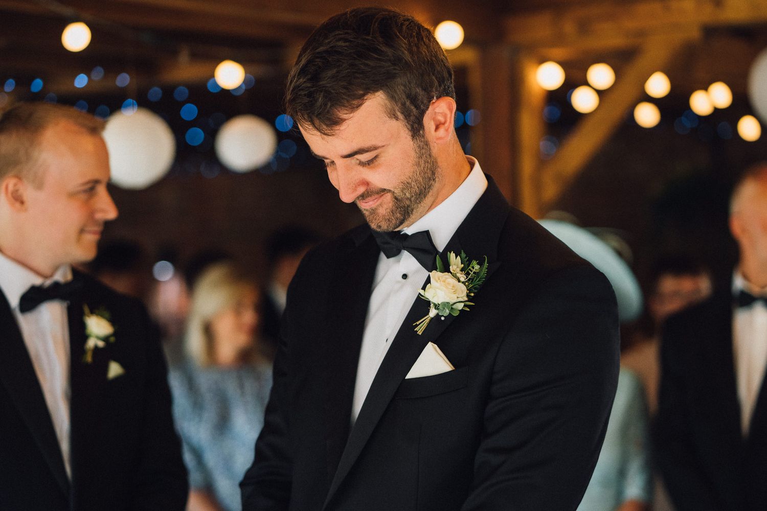 Wedding party members gather in an atmospheric barn setting with warm lighting and elegant details.