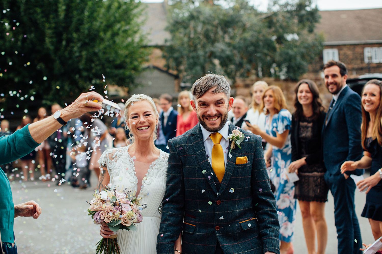 Wide shot of wedding party and guests celebrating with confetti outdoors.