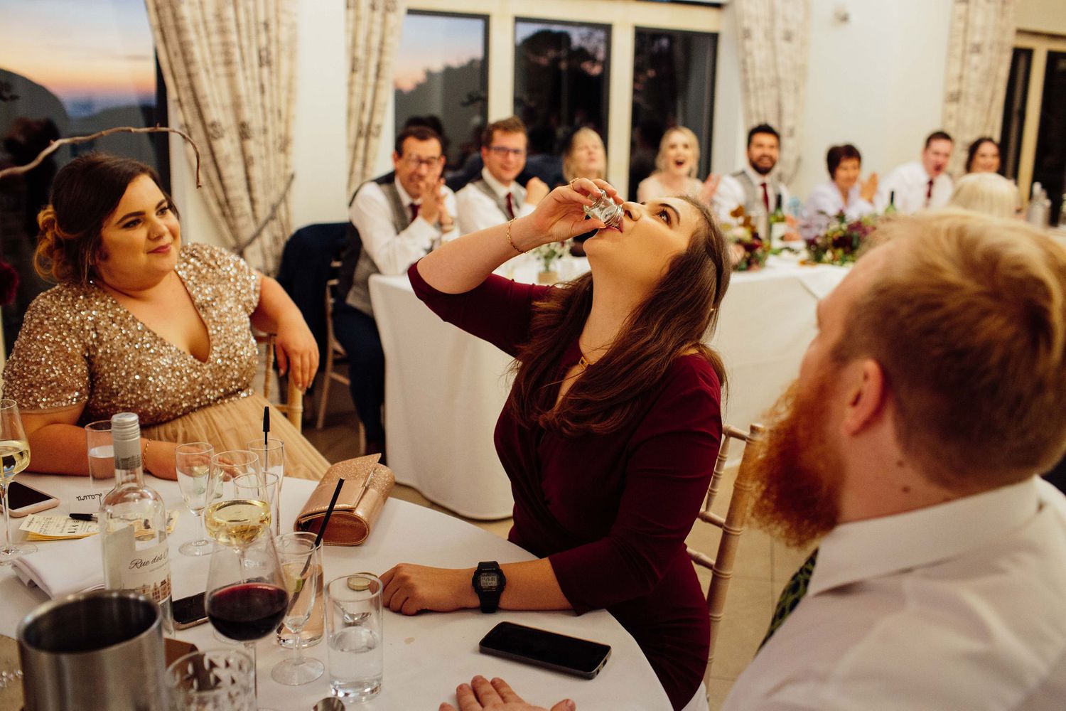 Wedding reception guests seated at long tables in an elegant dining room with warm lighting.