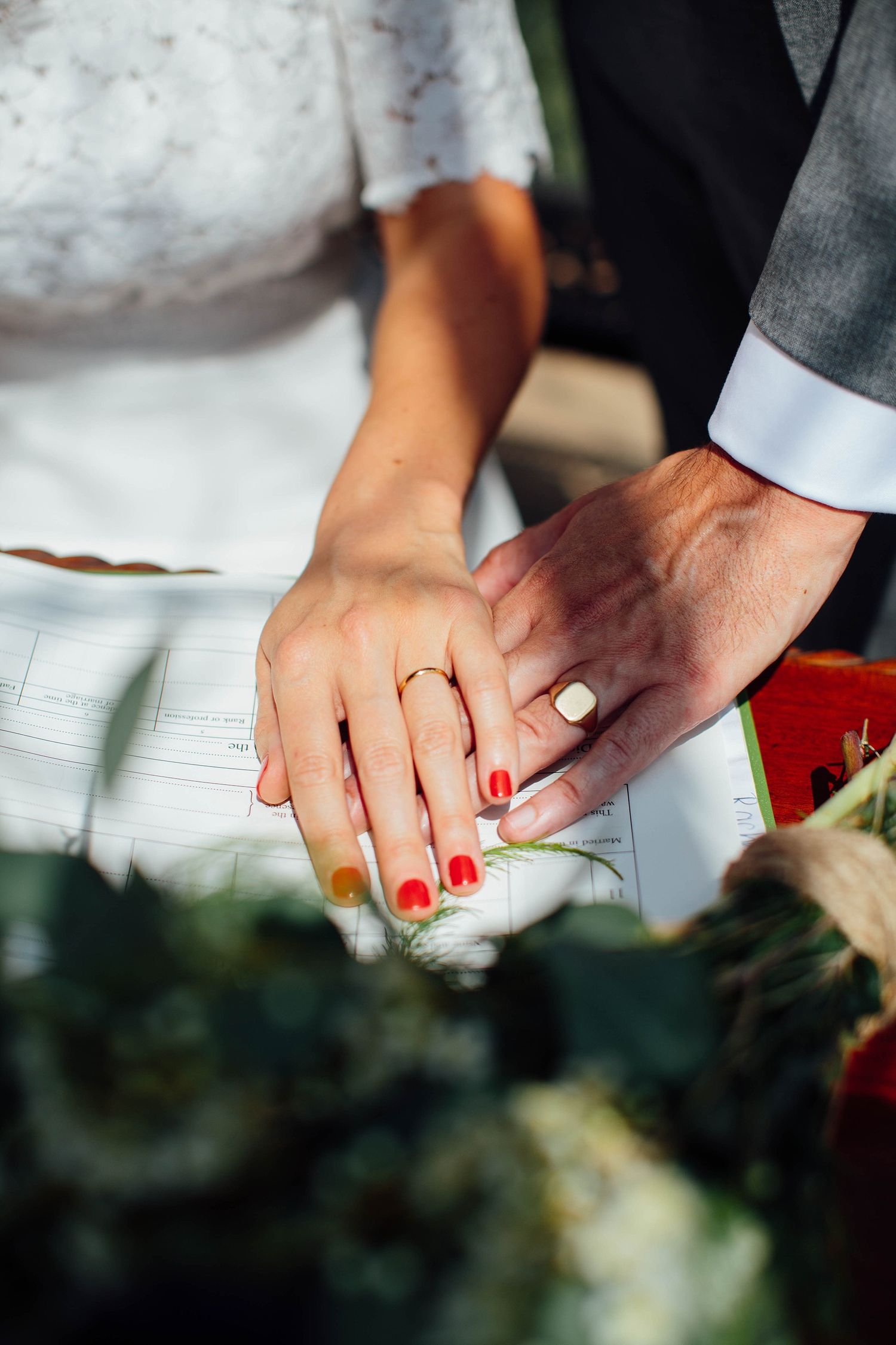 Close-up of hands exchanging rings during wedding ceremony with red nail polish detail.