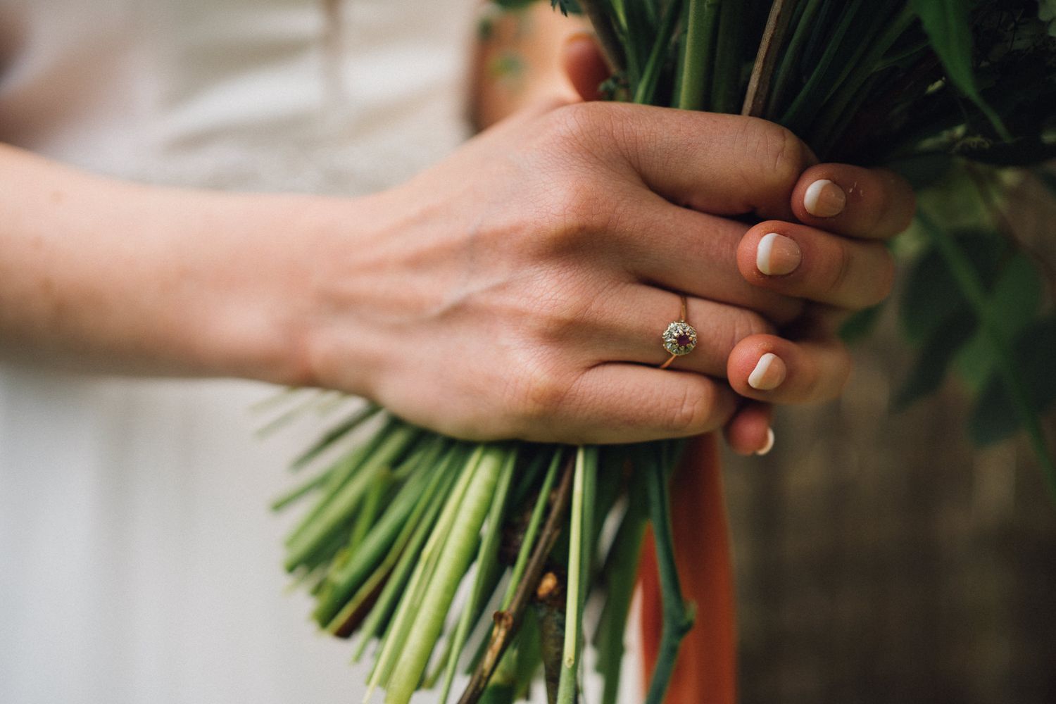 Close-up of hands holding a fresh white and green wedding bouquet.