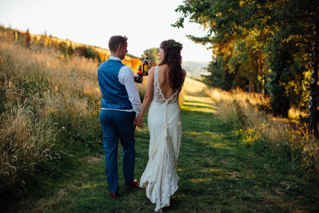 Wedding couple strolls through golden grass field at sunset.