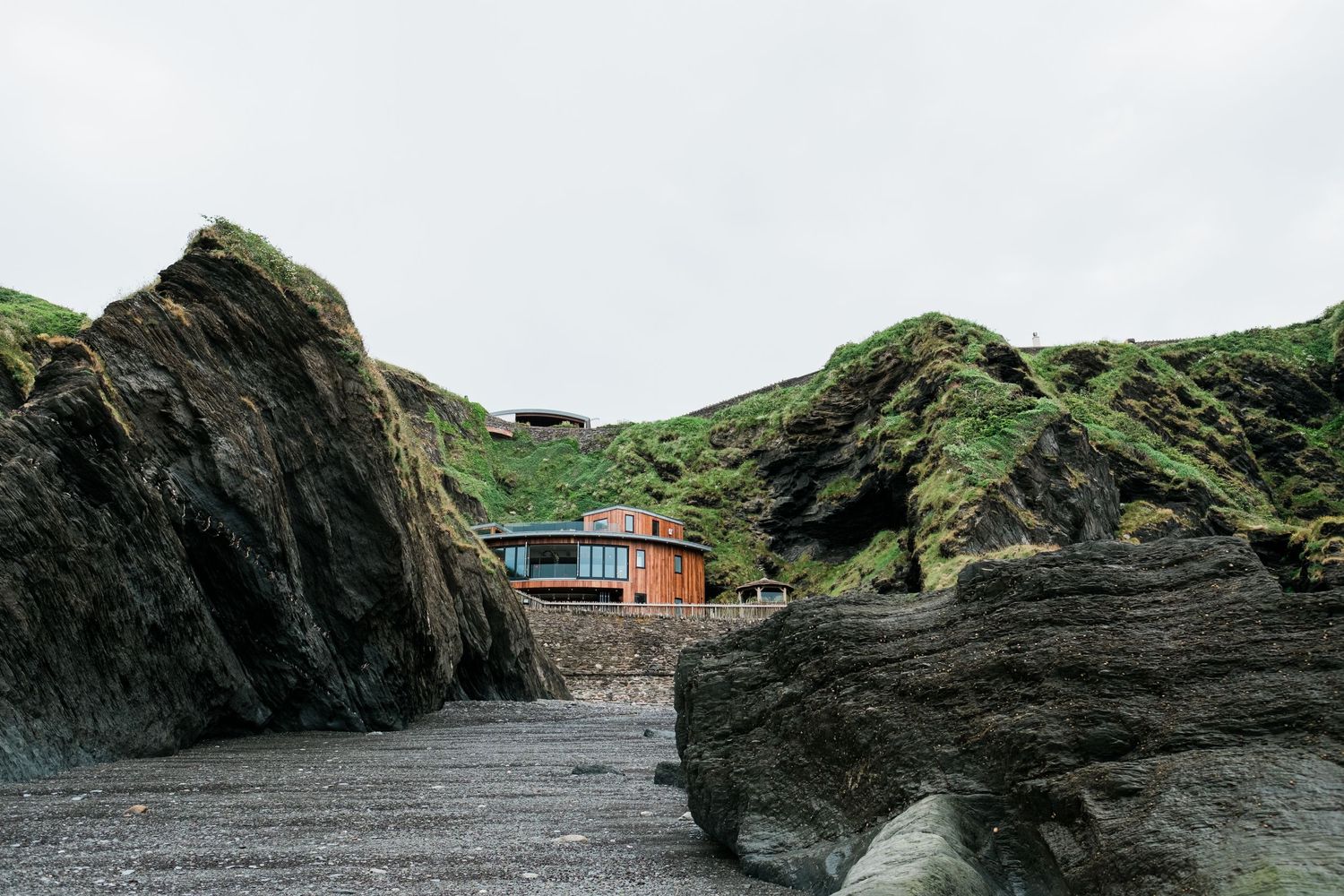 Rugged coastal landscape with modern house perched among green cliffs.