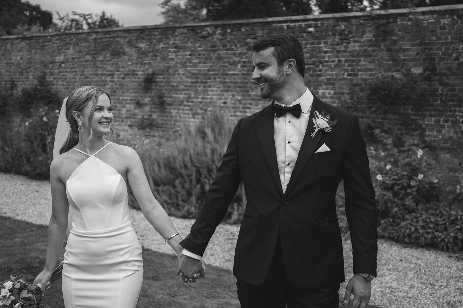 Black and white photo of newlyweds walking together against a vintage brick wall backdrop.