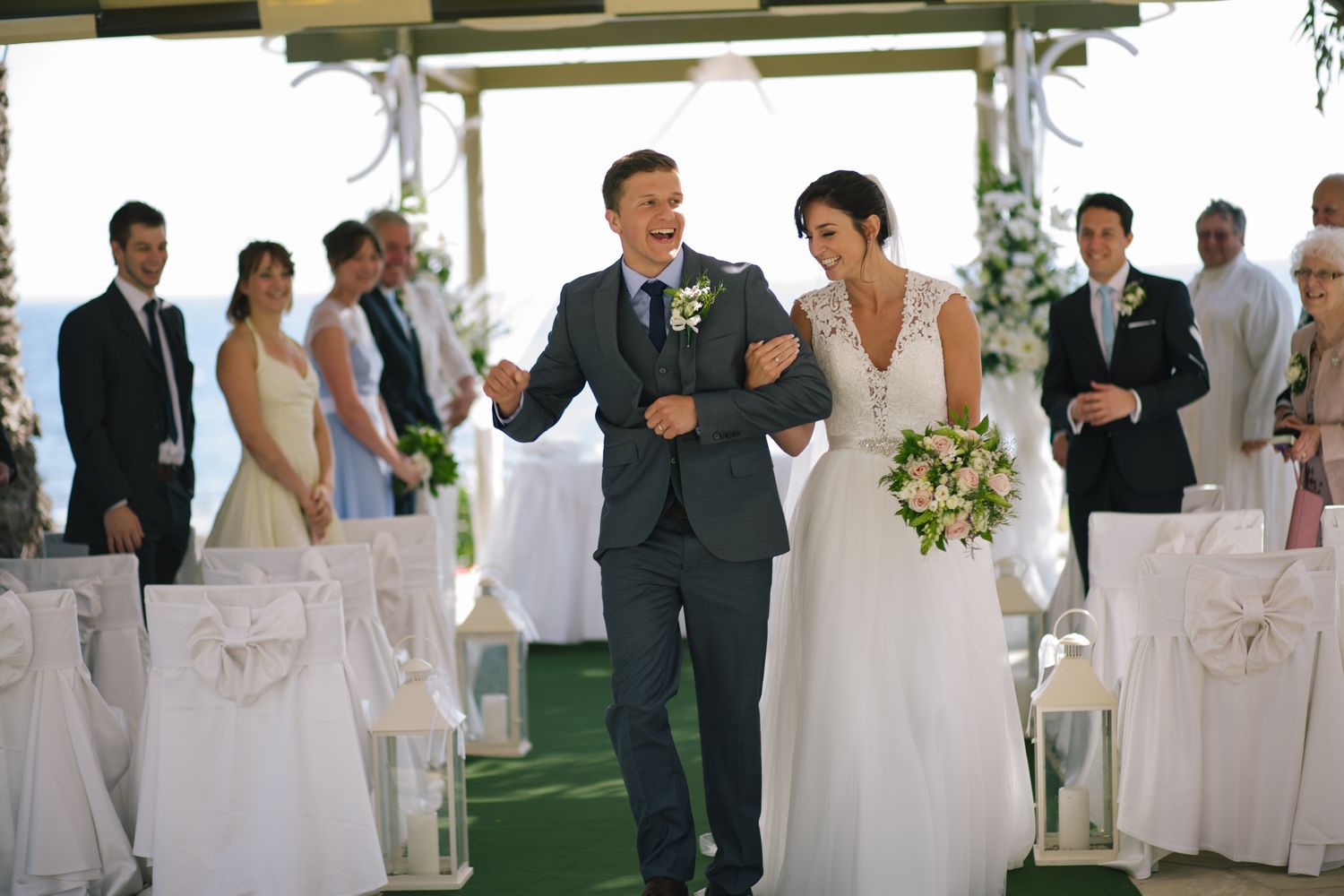 A joyful wedding ceremony exit as newlyweds walk down the aisle under a covered outdoor venue.