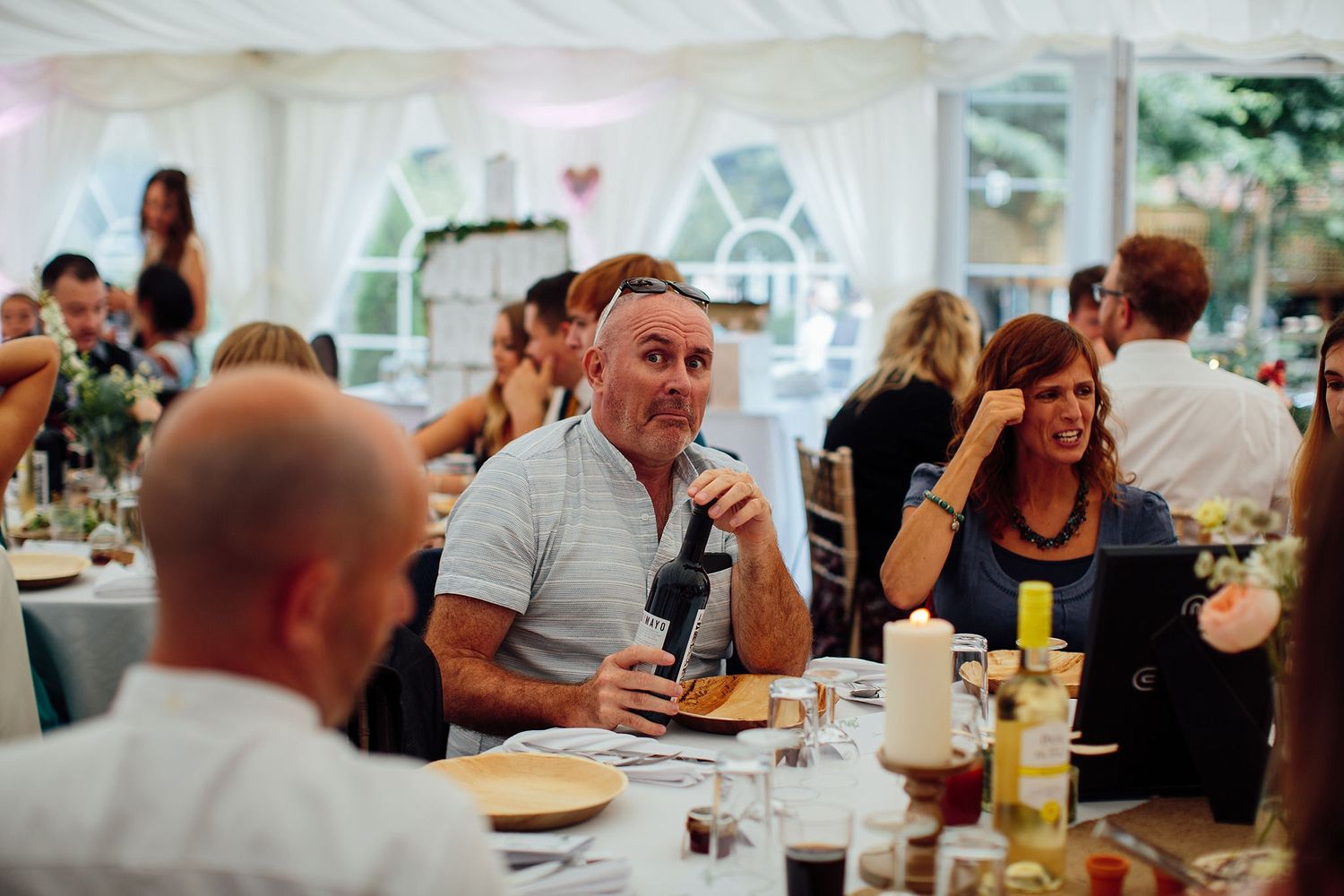Wedding reception dining area with guests seated at long tables inside a white tent.