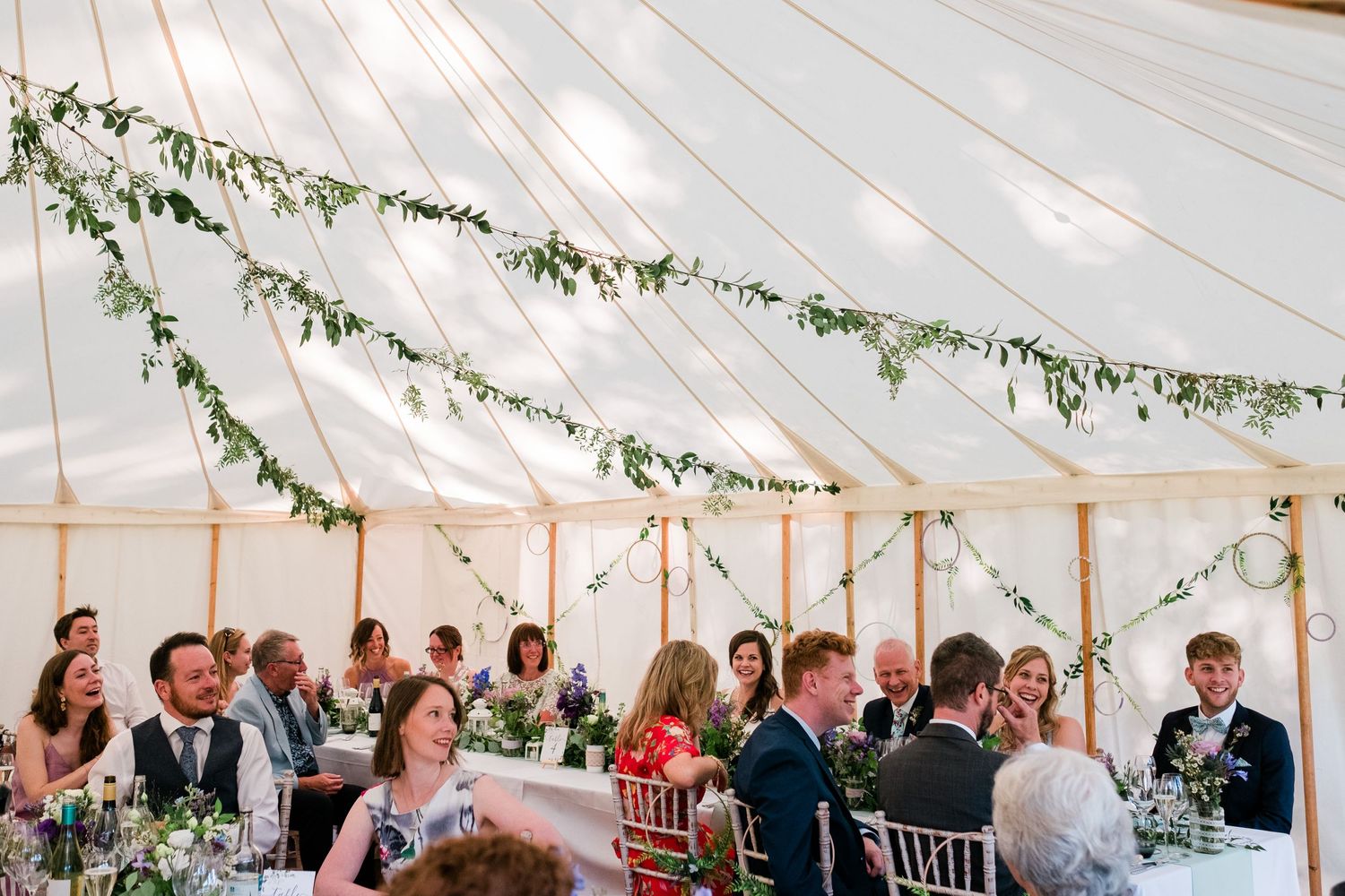 Interior of an elegant wedding tent with string lights and greenery decorations.