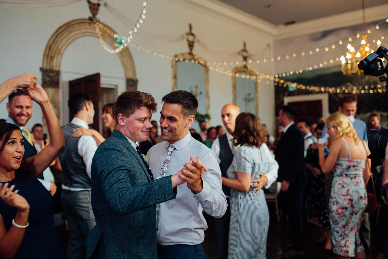 Wedding reception guests dancing and celebrating on a crowded dance floor under string lights.