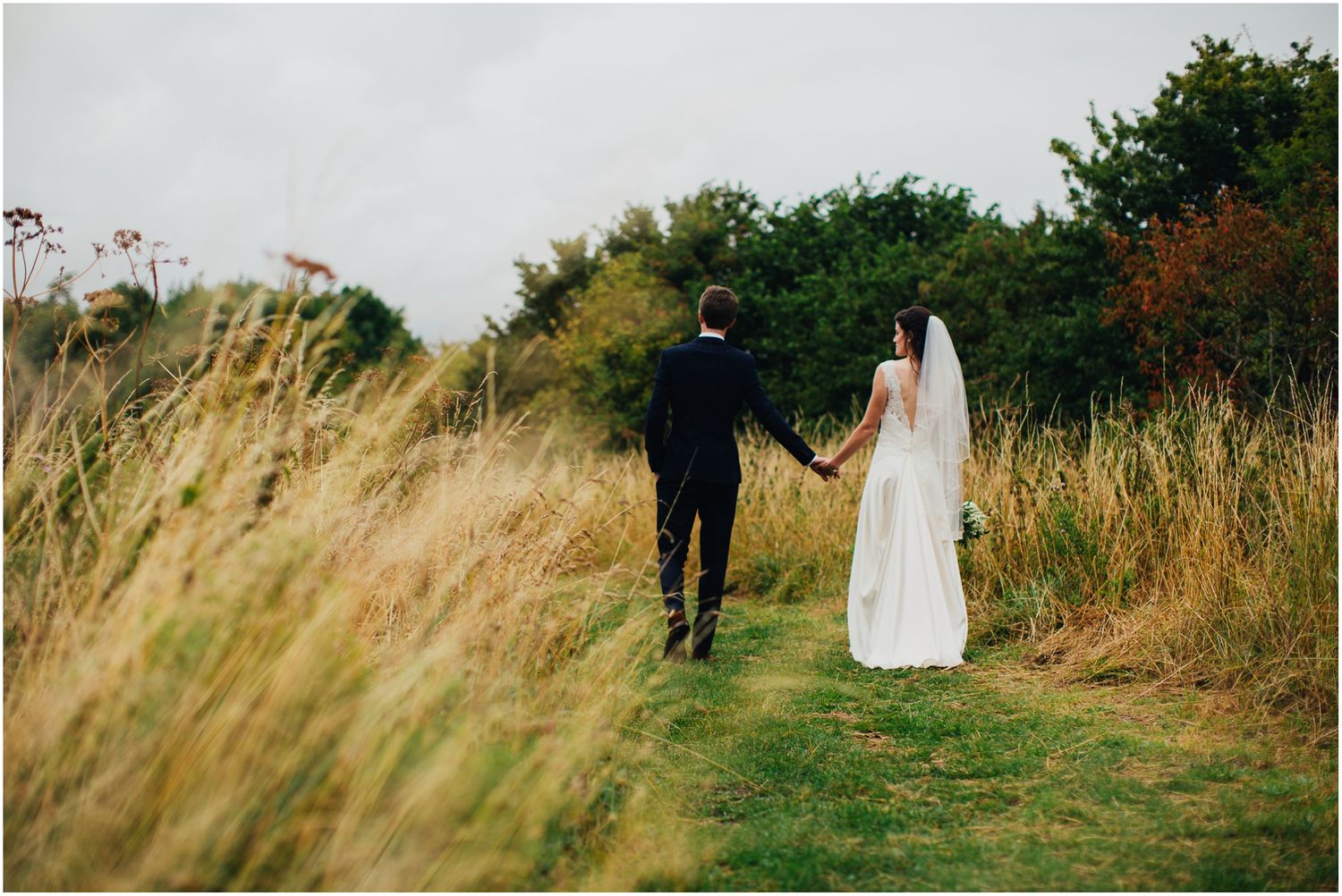 Newlyweds stroll through golden grass field during sunset photography session.
