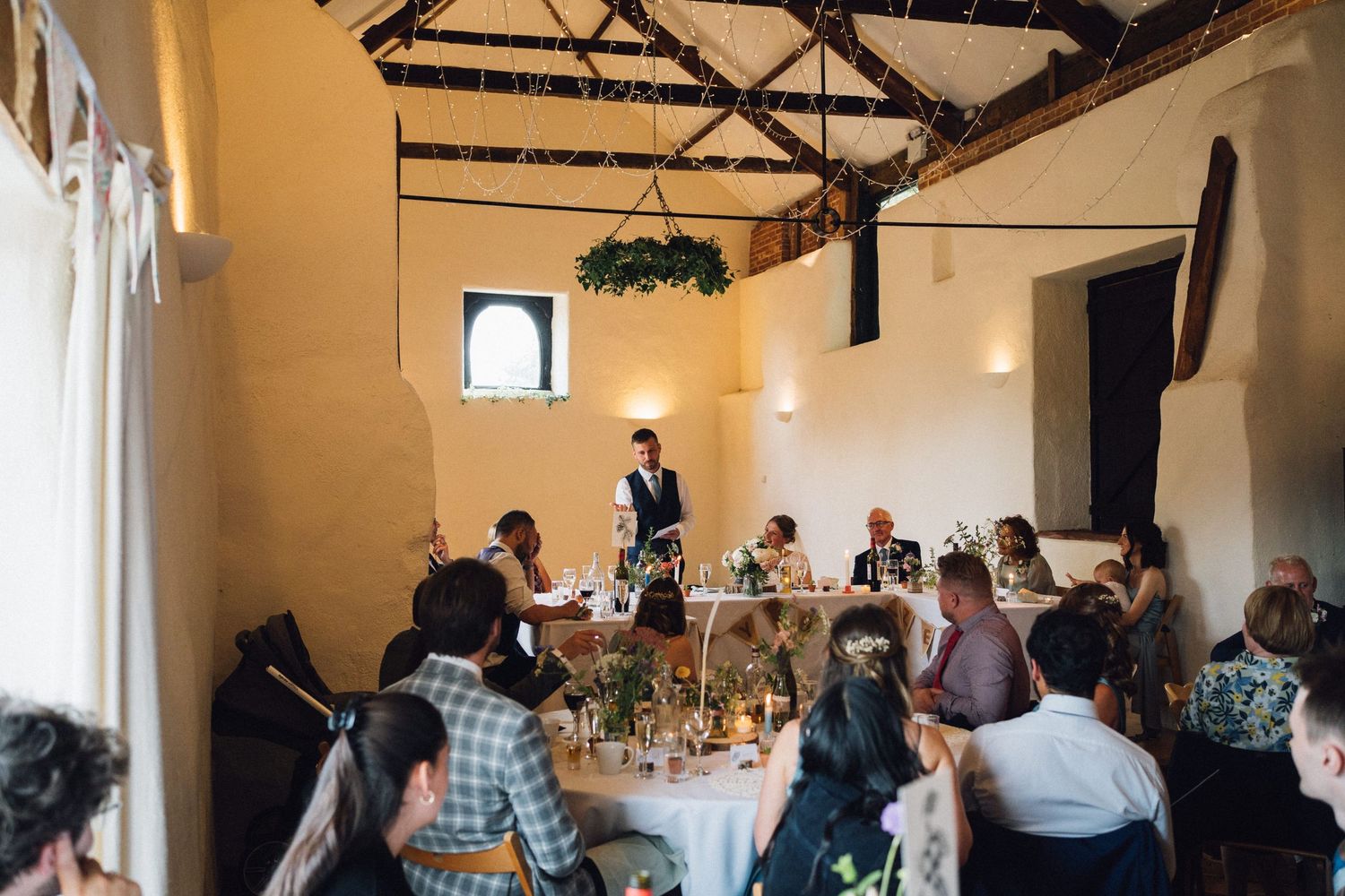 Wide angle view of wedding reception venue with exposed beams and white walls.
