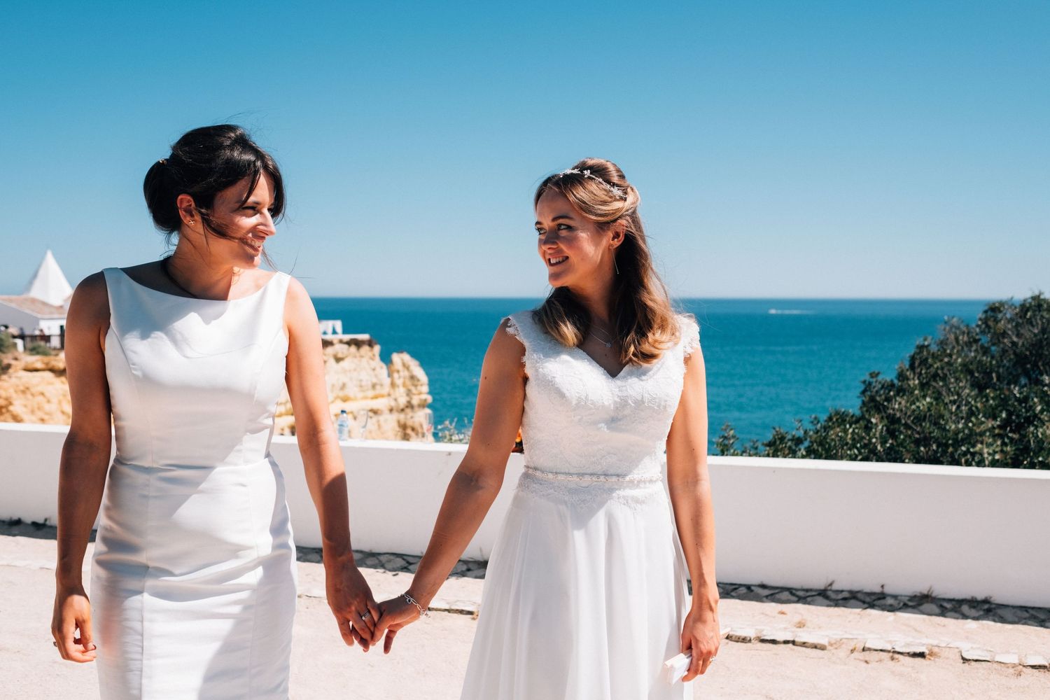 Outdoor wedding scene with white dresses against coastal backdrop.