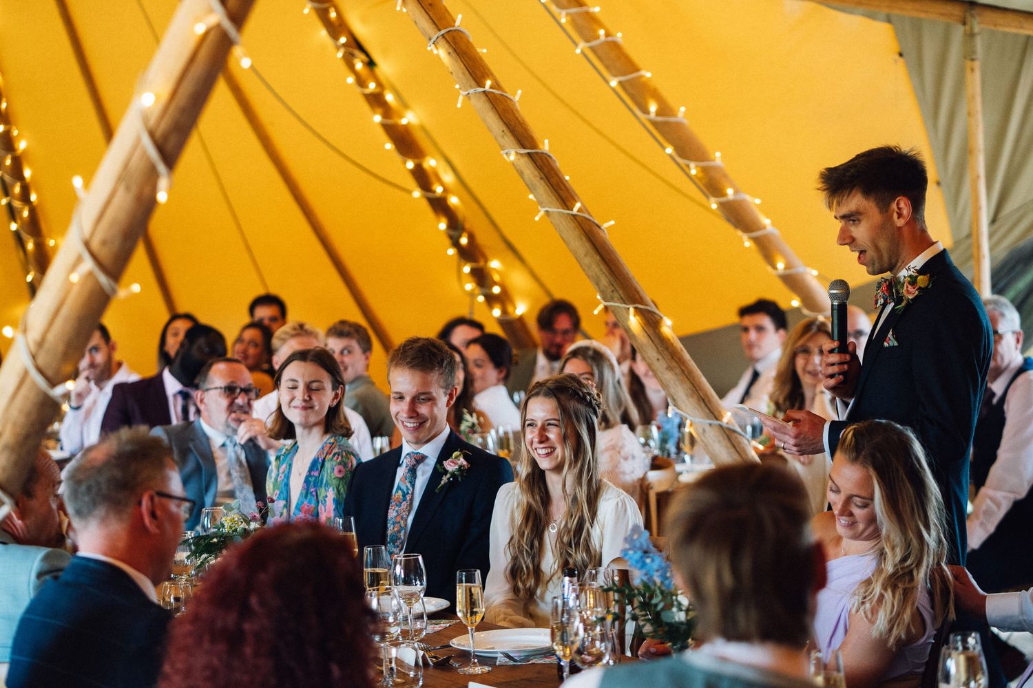 Wedding guests enjoying a reception celebration under a large yellow tent canopy.