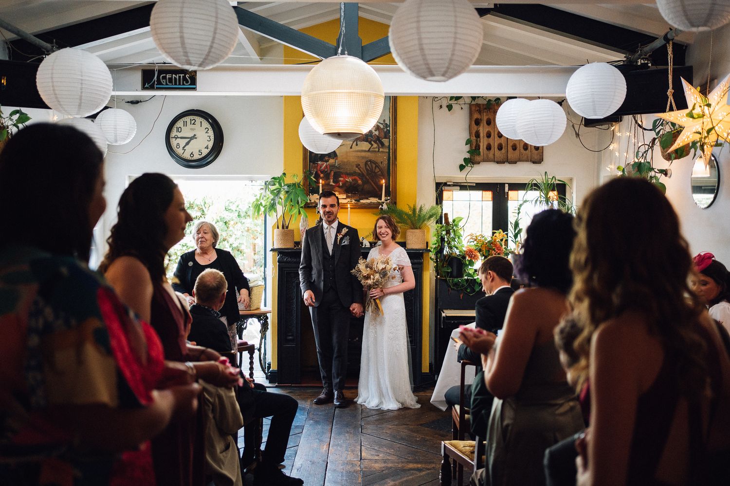 White paper lanterns and decorative lights illuminate a wedding reception venue with guests mingling in the background.