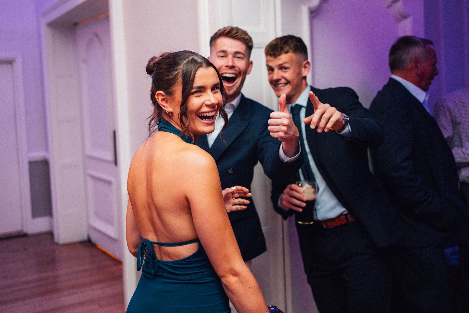 Wedding guests laugh and dance together during an energetic reception celebration under purple lighting.