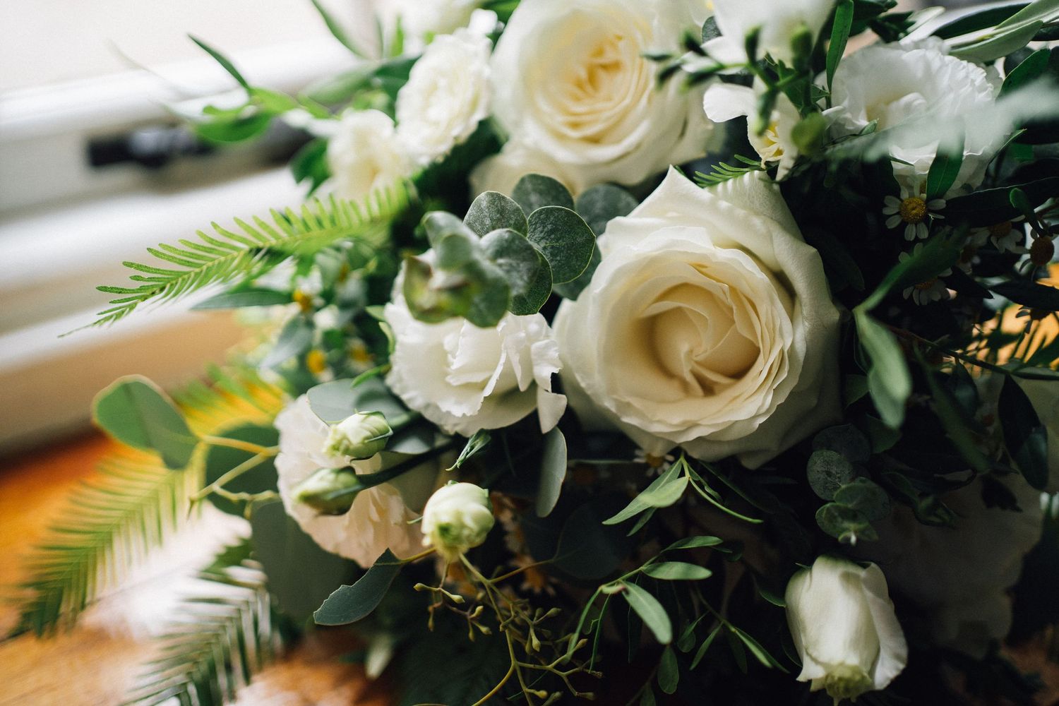 Elegant white roses and greenery arranged in a wedding bouquet with delicate ferns and foliage.