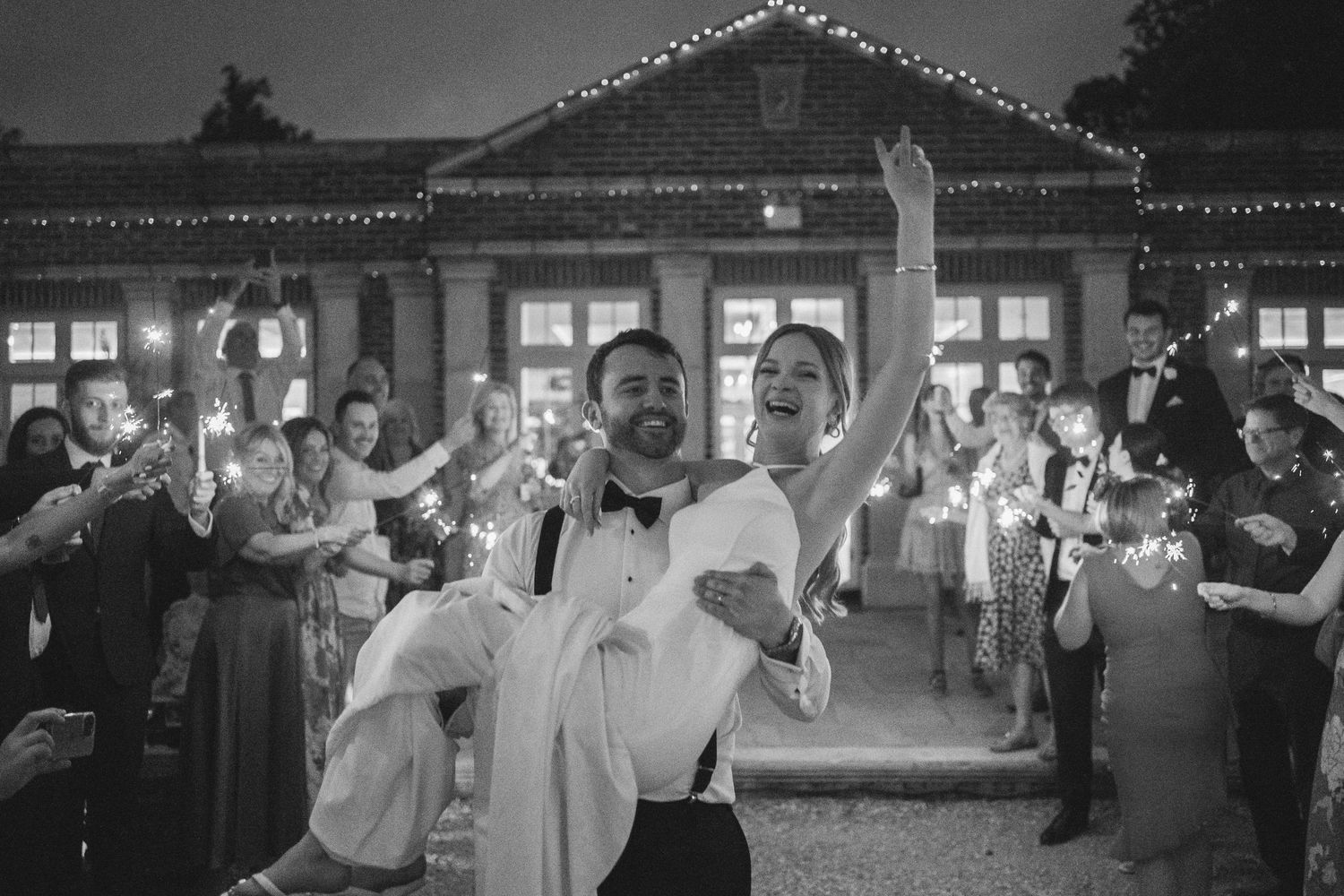 Black and white photo of wedding reception party with string lights and dancing guests.