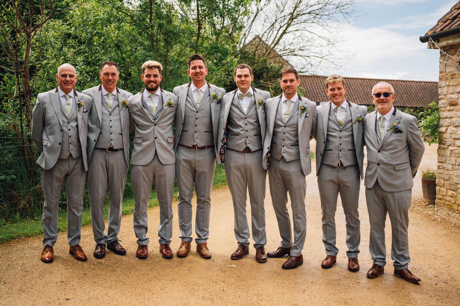 Wedding party in matching gray suits and sunglasses pose together outdoors in a series of candid group photos.