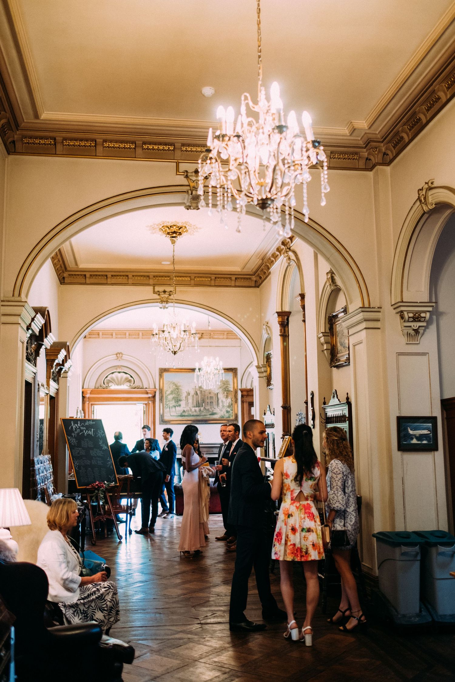 Elegant hallway with crystal chandeliers and arched doorways during a formal event with guests mingling.